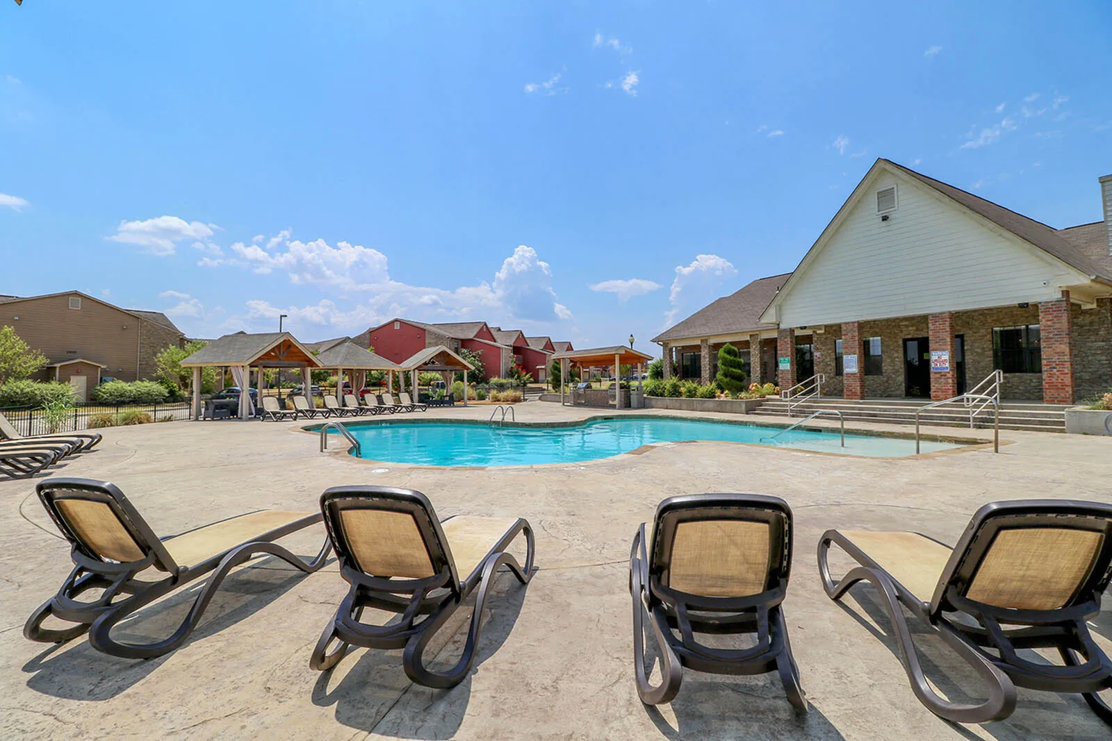 Inviting outdoor pool area with comfortable lounge chairs, surrounded by charming wooden pavilions and vibrant landscaping under a bright blue sky.
