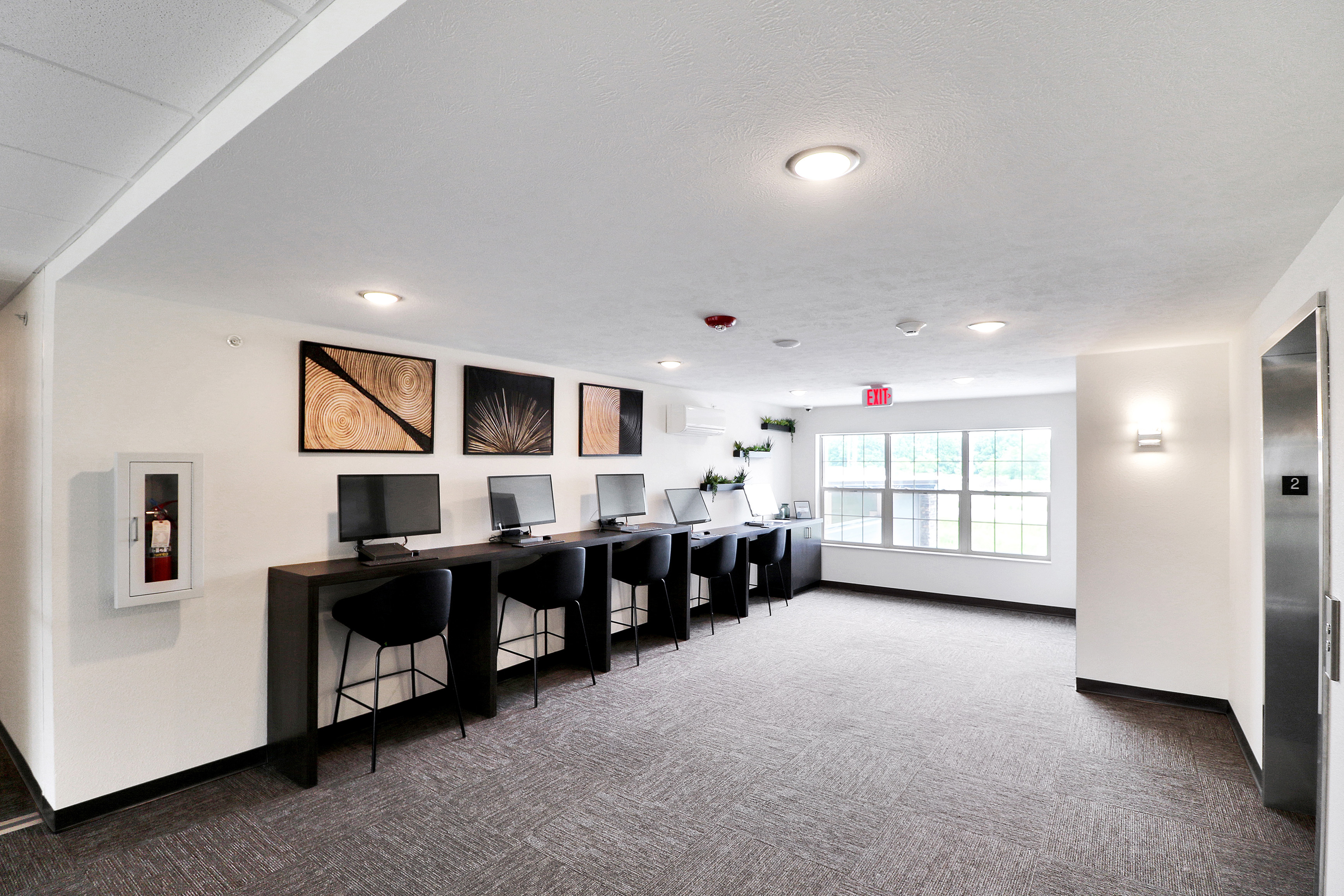 Modern communal workspace featuring sleek computer stations, contemporary artwork, and large windows for natural light.