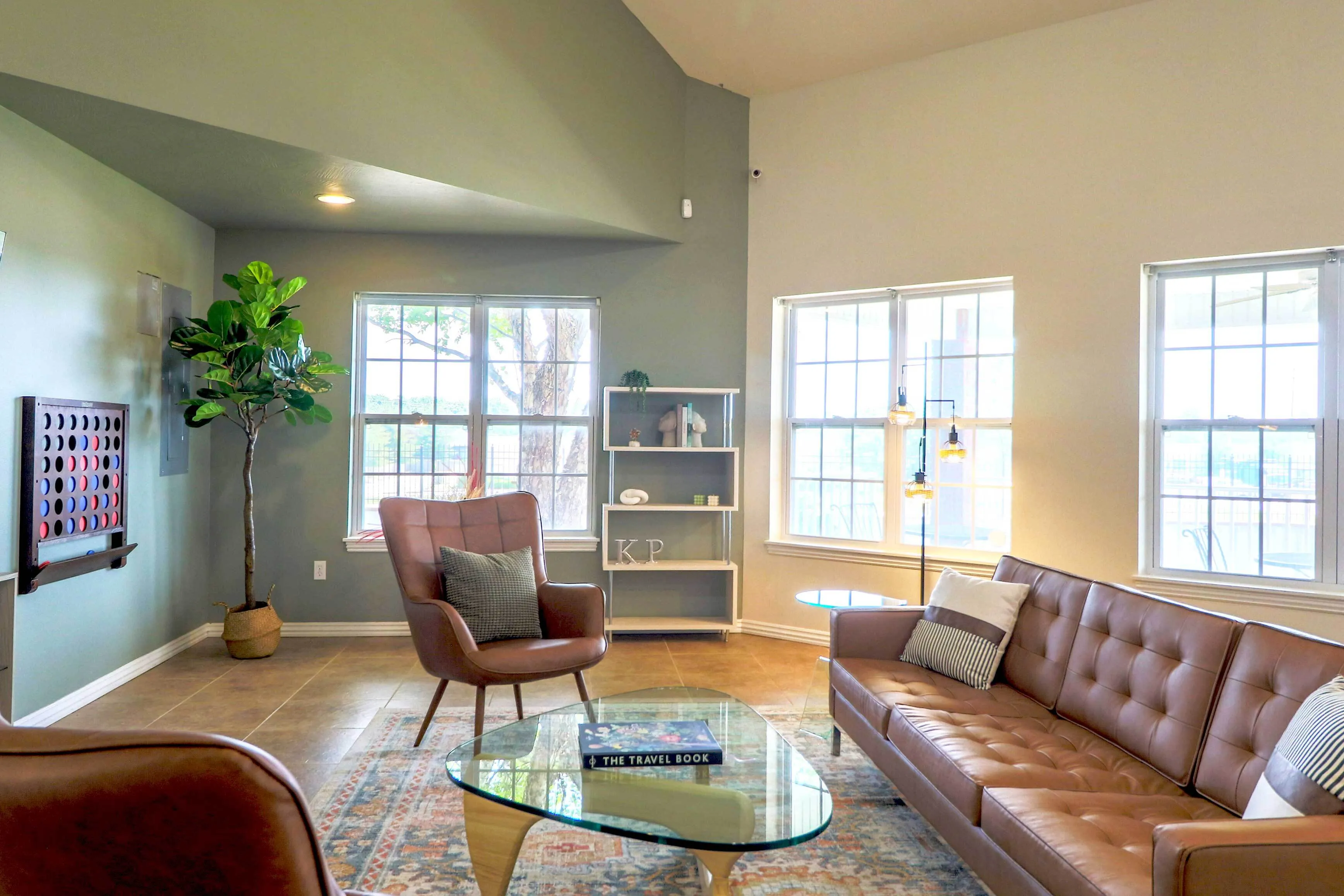 Bright and inviting living room with large windows, sleek brown leather furniture, modern decor, and a cozy atmosphere.