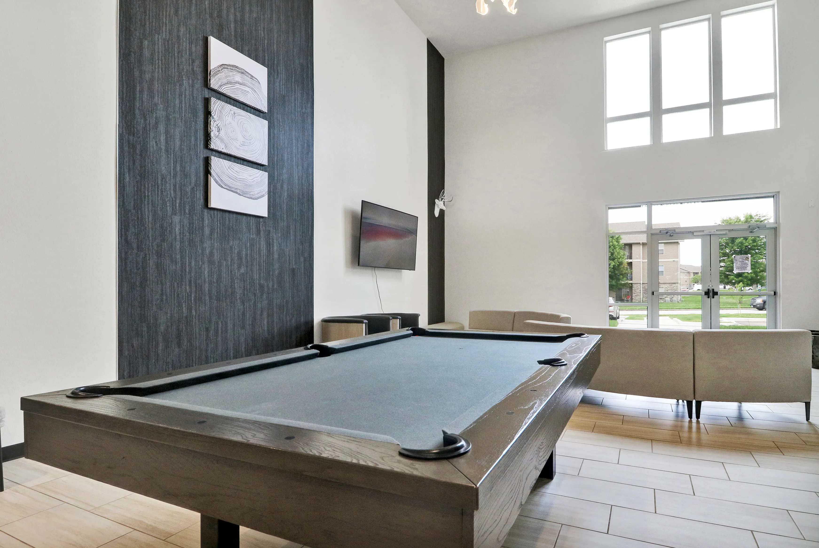 Modern lounge with high ceilings featuring a sleek pool table, comfortable seating, and large windows offering natural light.
