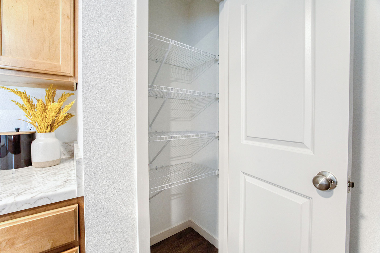Inviting pantry space with sleek wire shelving, adjacent to a stylish marble countertop accented by vibrant yellow decor.