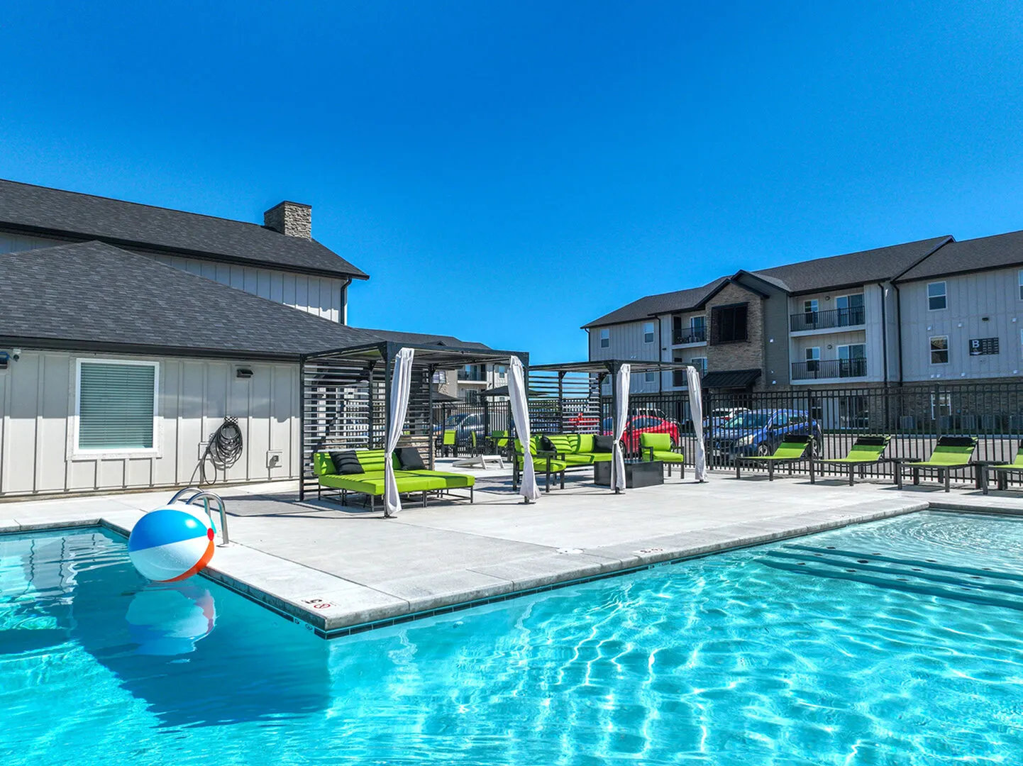 Chic apartment complex featuring a vibrant outdoor pool area with modern lounge chairs and a sunlit patio, perfect for relaxation.