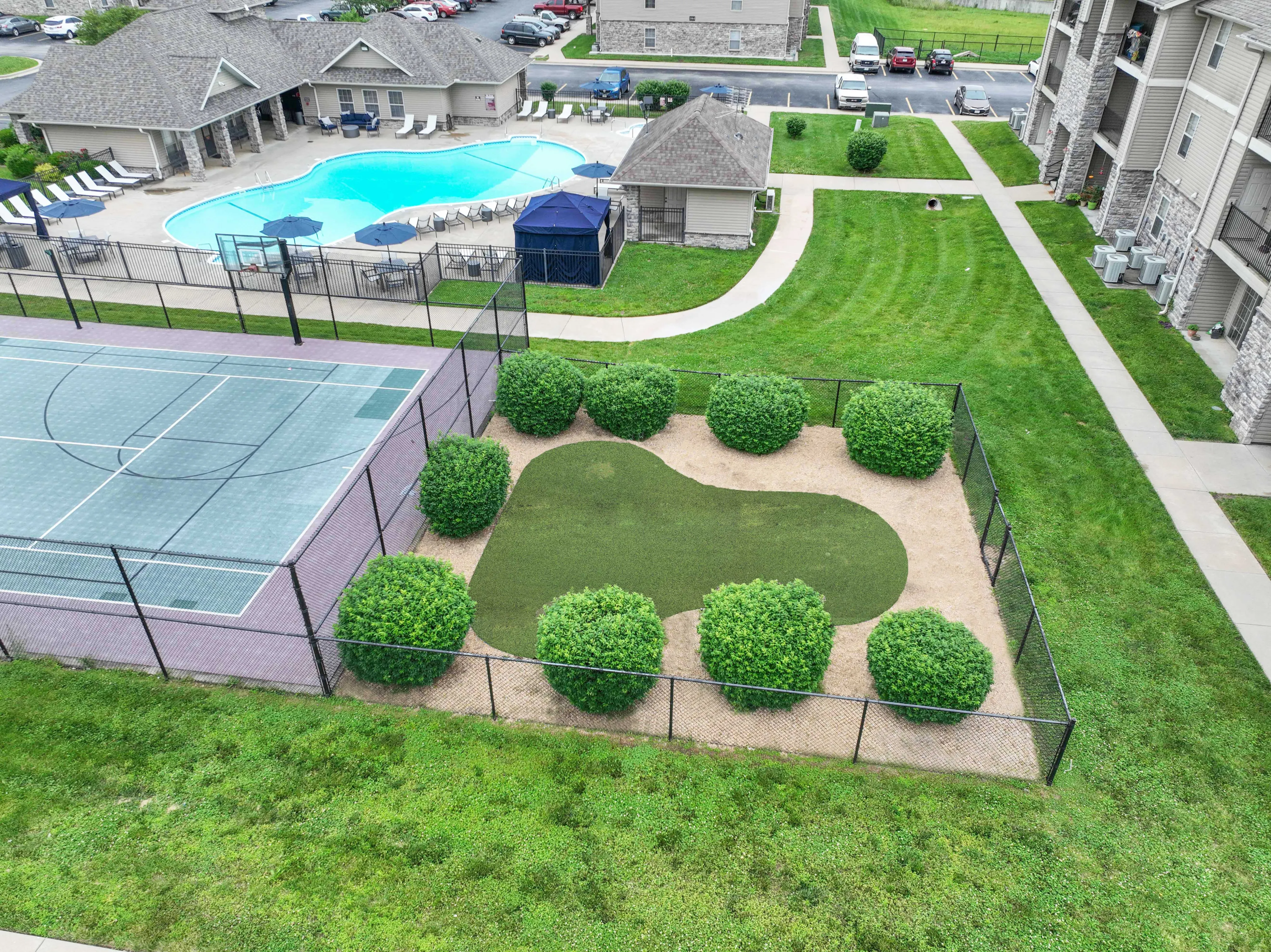 Inviting residential area featuring a pristine swimming pool, tennis court, and lush green landscaping, perfect for active and relaxed lifestyles.