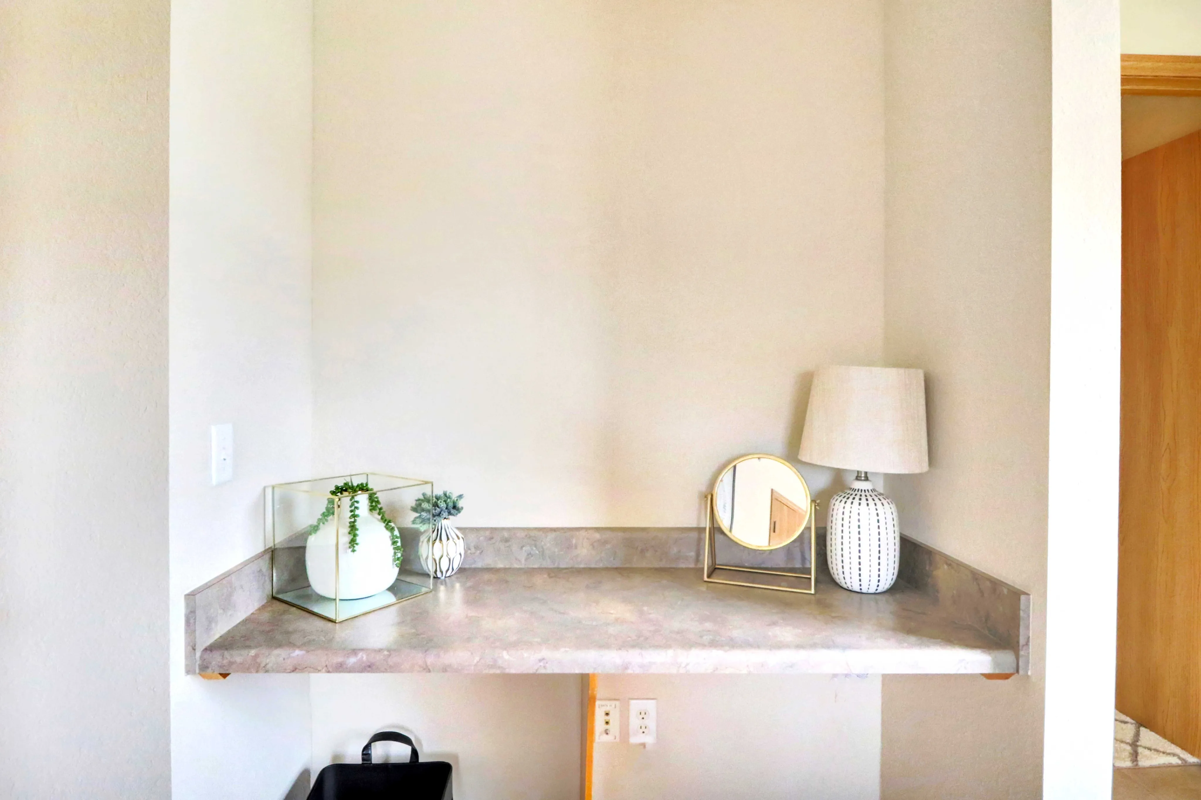 Chic corner space with elegant decor featuring a sleek countertop, mirror, stylish lamp, and decorative plants, enhancing modern apartment aesthetics.