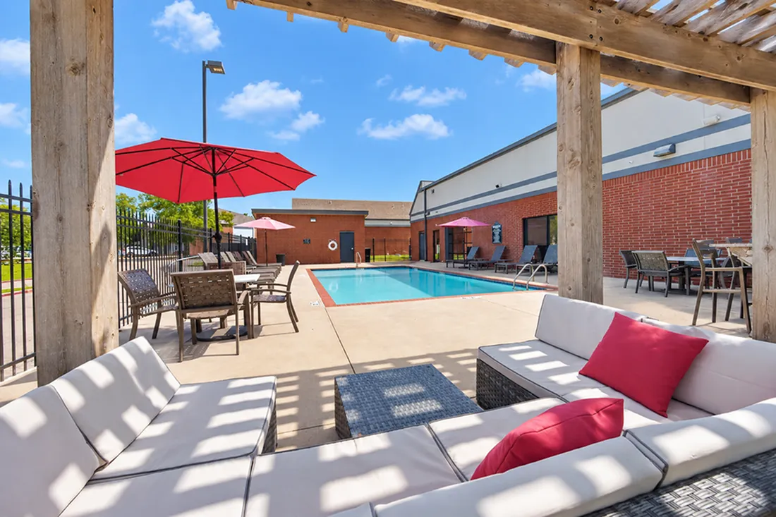 Inviting outdoor pool area with chic lounge seating and vibrant red umbrellas under a clear blue sky, perfect for relaxation and entertaining.