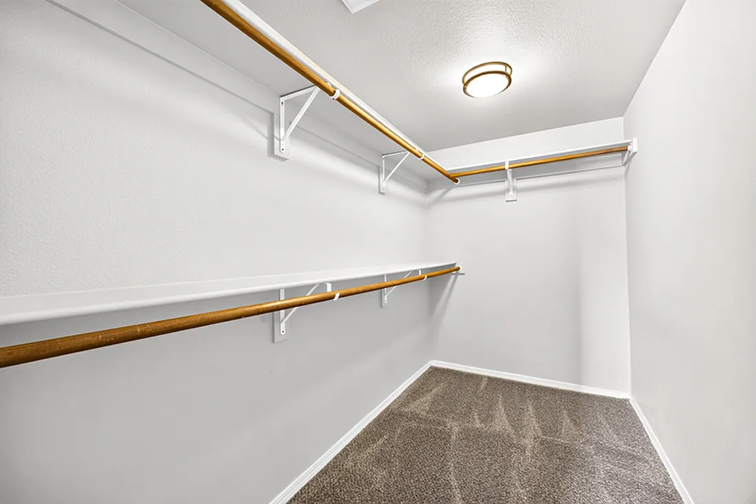 Spacious walk-in closet with elegant wooden rods and plush carpet floor, ideal for ample storage.