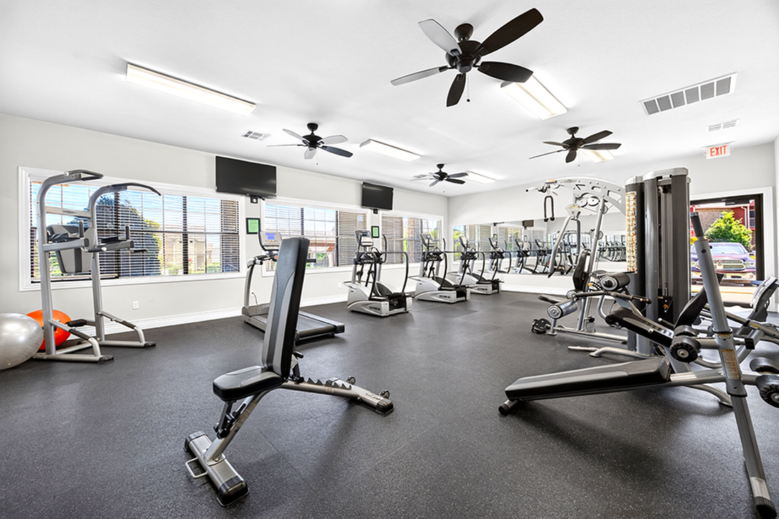 Modern fitness center with various gym equipment, including treadmills, exercise bikes, and weight machines in a spacious, well-lit room.