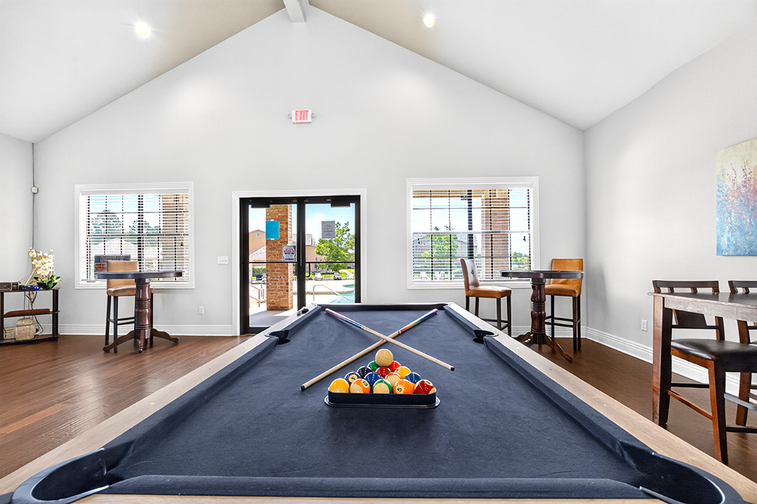 Bright and inviting recreation room featuring a sleek pool table, ample natural light, and stylish bar seating, perfect for relaxation and entertainment.