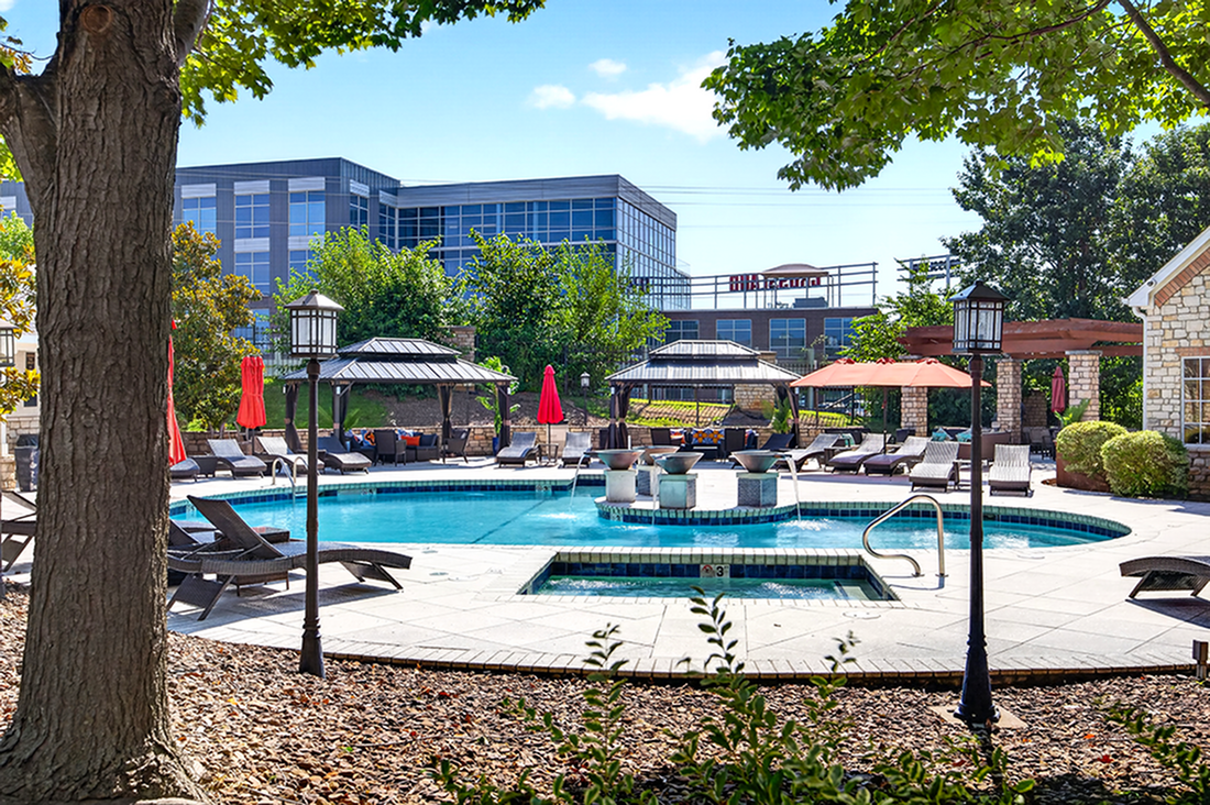 Luxurious apartment complex featuring a resort-style pool area with stylish loungers, vibrant red umbrellas, and lush greenery for a tranquil escape.