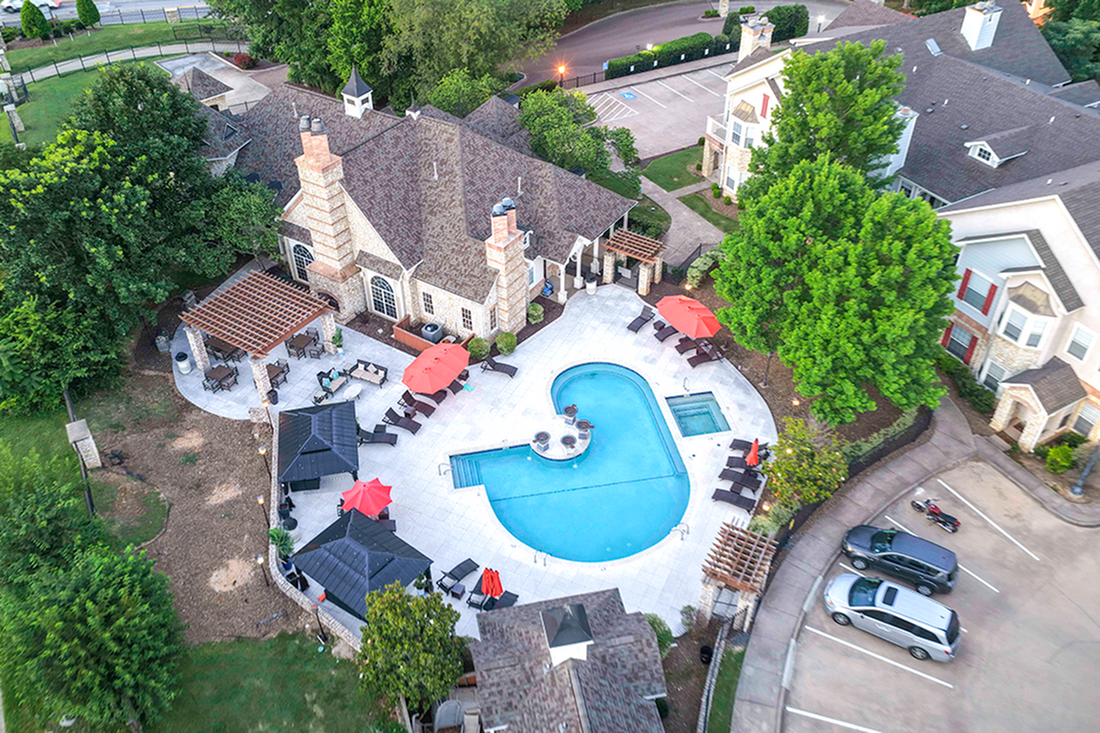 Breathtaking aerial view of luxurious apartment complex showcasing a stylish pool area with lounge chairs, vibrant umbrellas, and lush greenery.