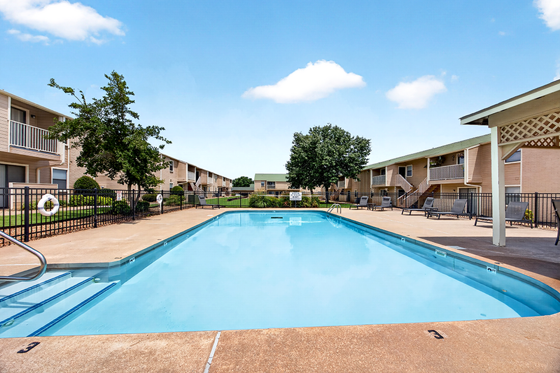 Inviting apartment complex with a sparkling swimming pool, lush green landscaping, and comfortable sun loungers.
