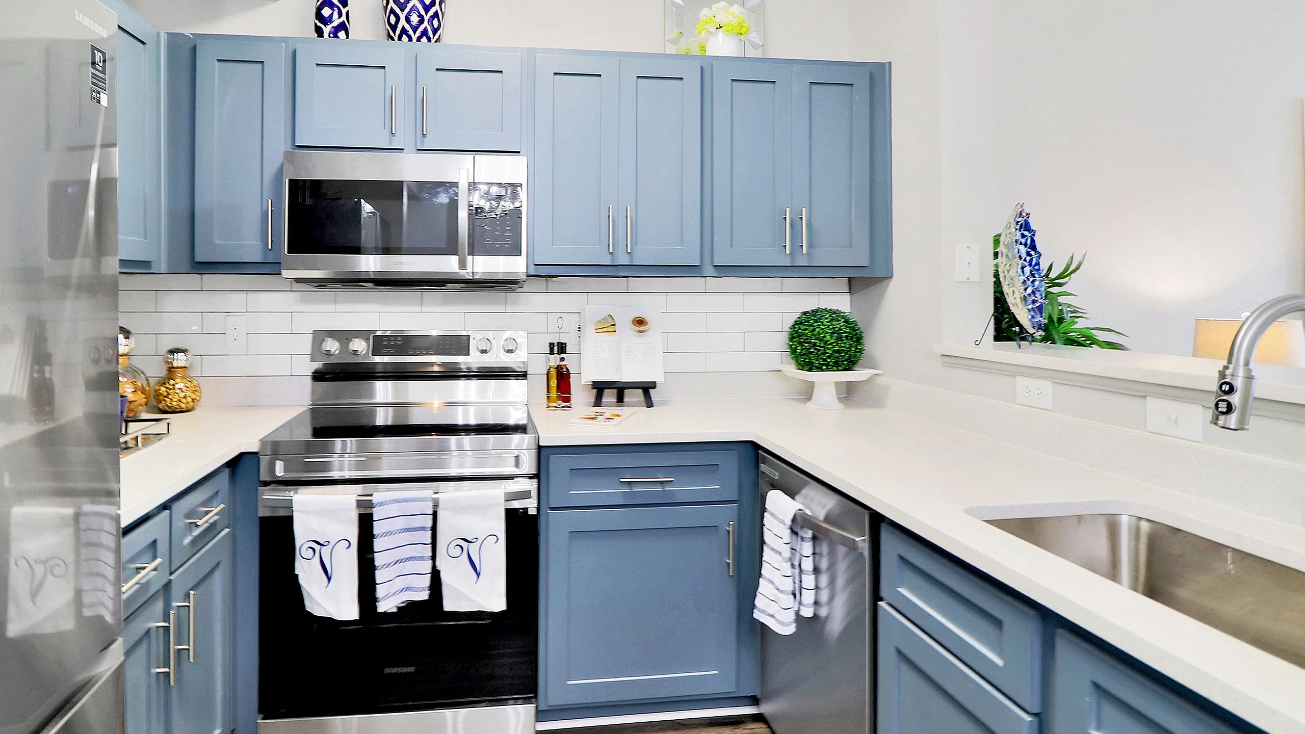 Elegant modern kitchen with sleek stainless steel appliances, stylish blue cabinetry, and bright countertops for a luxurious cooking experience.