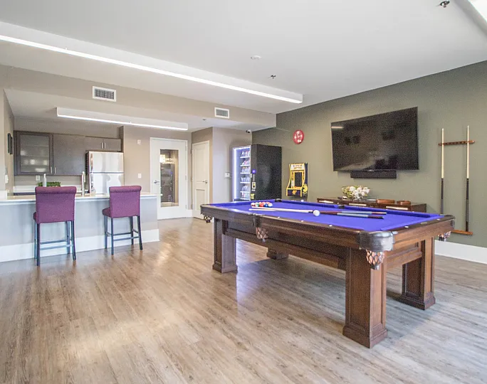 Chic entertainment room featuring a stylish billiards table, cozy bar seating, and a large wall-mounted TV.
