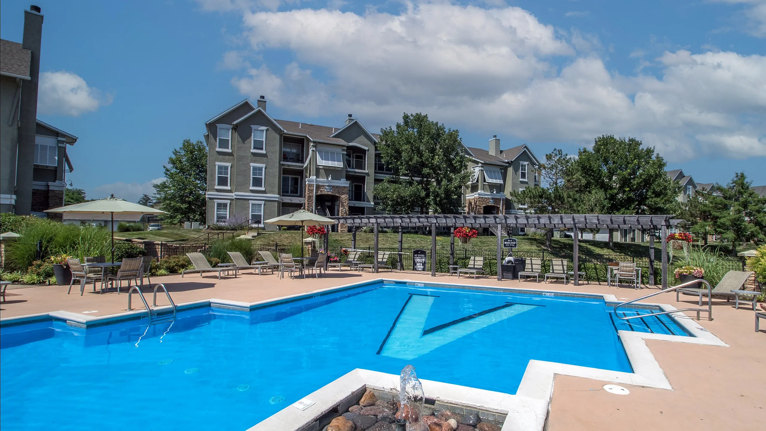 Charming apartment complex with a refreshing pool, relaxing lounge chairs, and a landscaped garden, perfect for summer enjoyment.