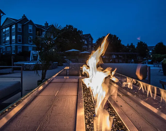 Luxurious outdoor fire pit with elegant seating and cozy ambiance in upscale apartment complex at dusk.