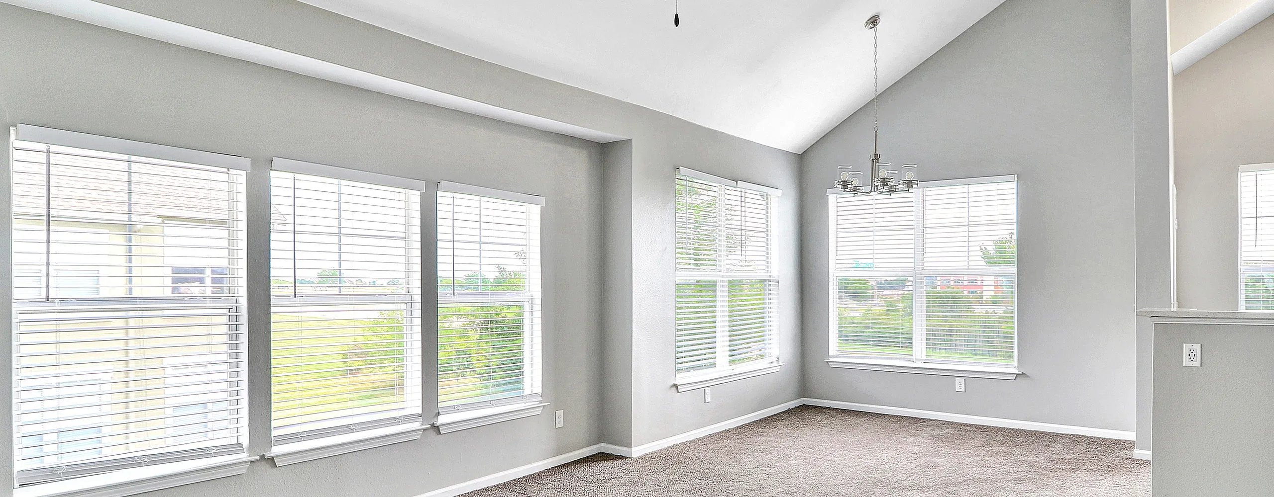 Sunlit corner room with vaulted ceilings, modern ceiling fan, and expansive windows offering tranquil views.