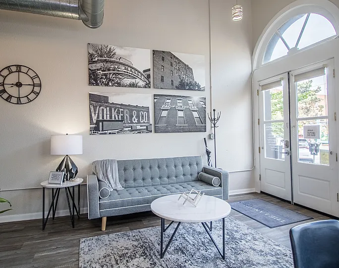 Bright and inviting living room with a sleek gray sofa, modern wall art, large windows, and elegant decor, perfect for a cozy urban lifestyle.