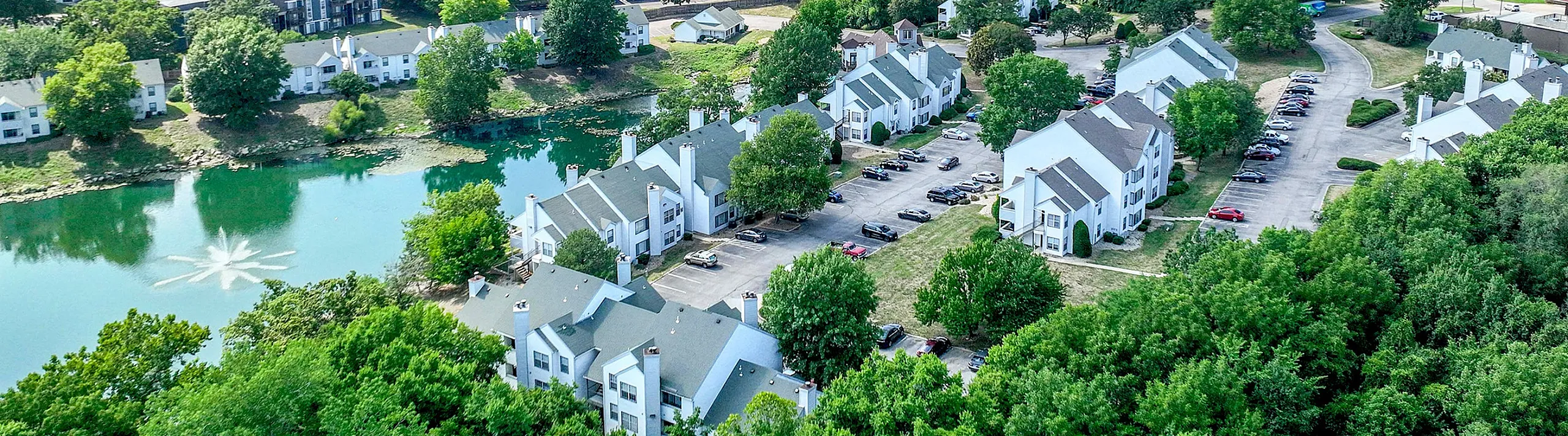 Scenic aerial view of a serene residential community featuring charming white houses surrounded by lush greenery and a picturesque pond.