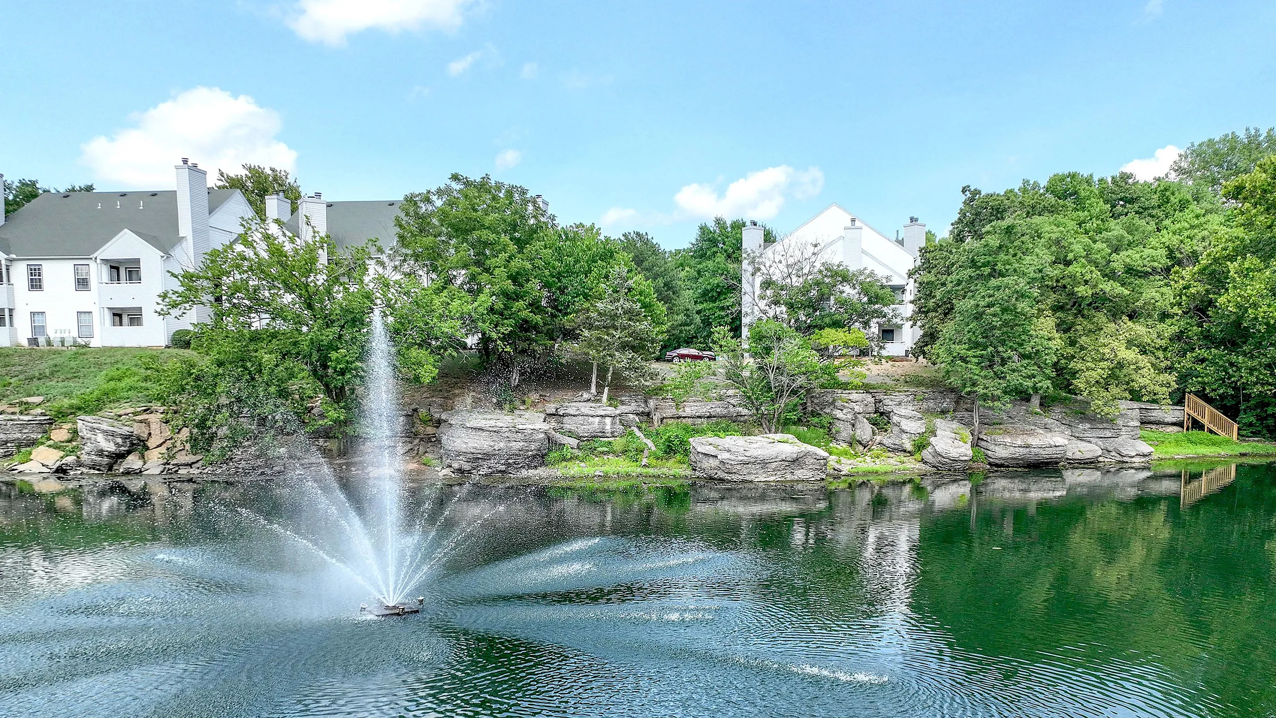 Serene lakeside view with a beautiful water fountain and lush greenery, perfect for tranquil living.