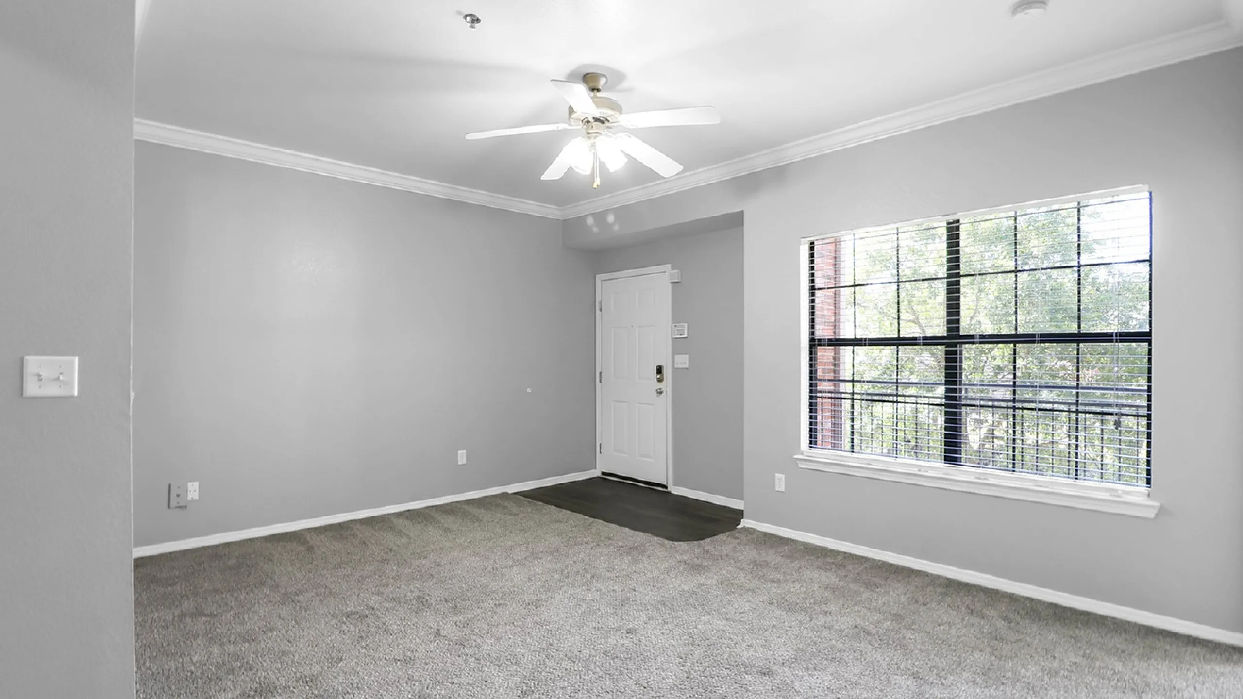 Bright and inviting living space with fresh gray walls, plush carpet, and large window offering natural light.