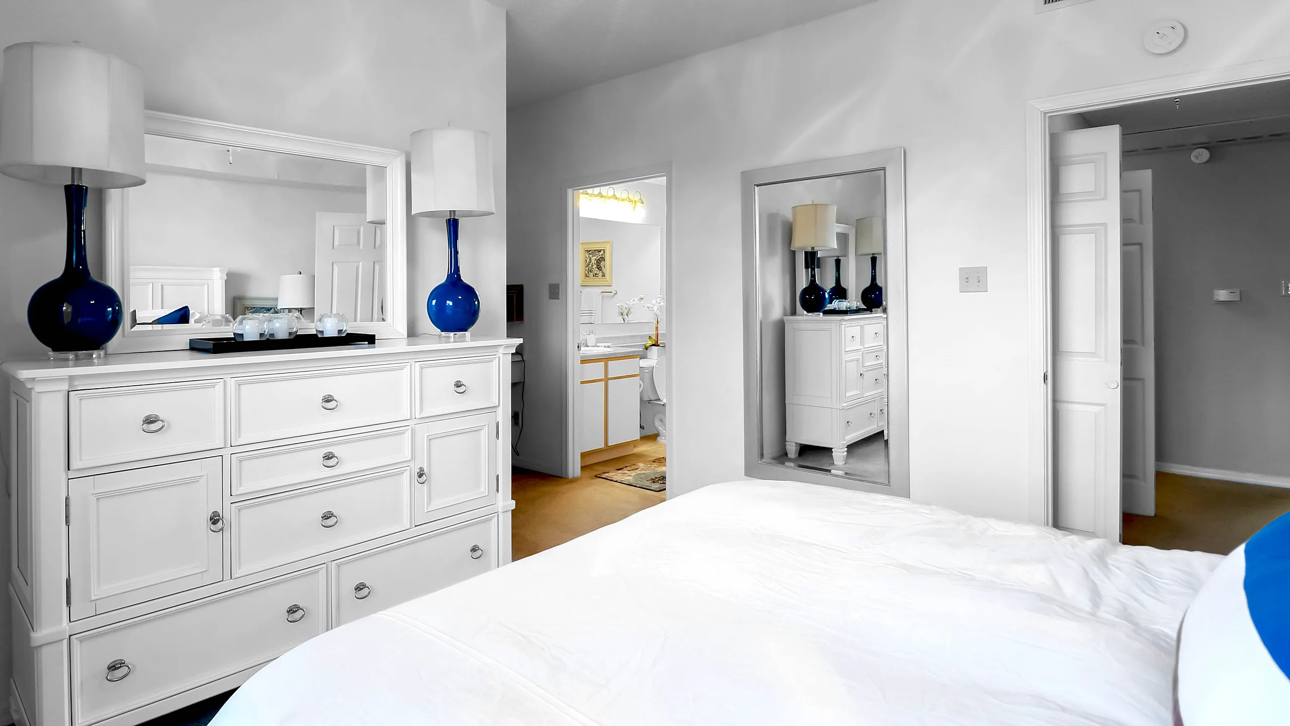 Elegant bedroom showcasing a bright white dresser with chic blue vases, softly lit by a modern ceiling chandelier.
