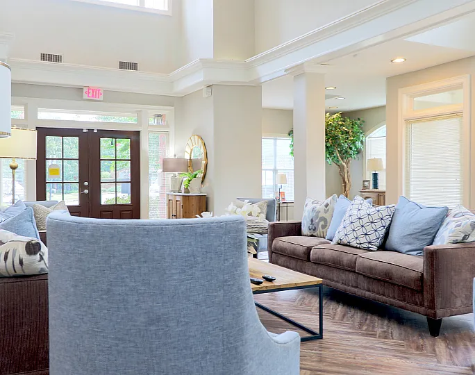 Bright and inviting living room with high ceilings, elegant sofas adorned with plush cushions, and a large window letting in natural light, creating a cozy ambiance.