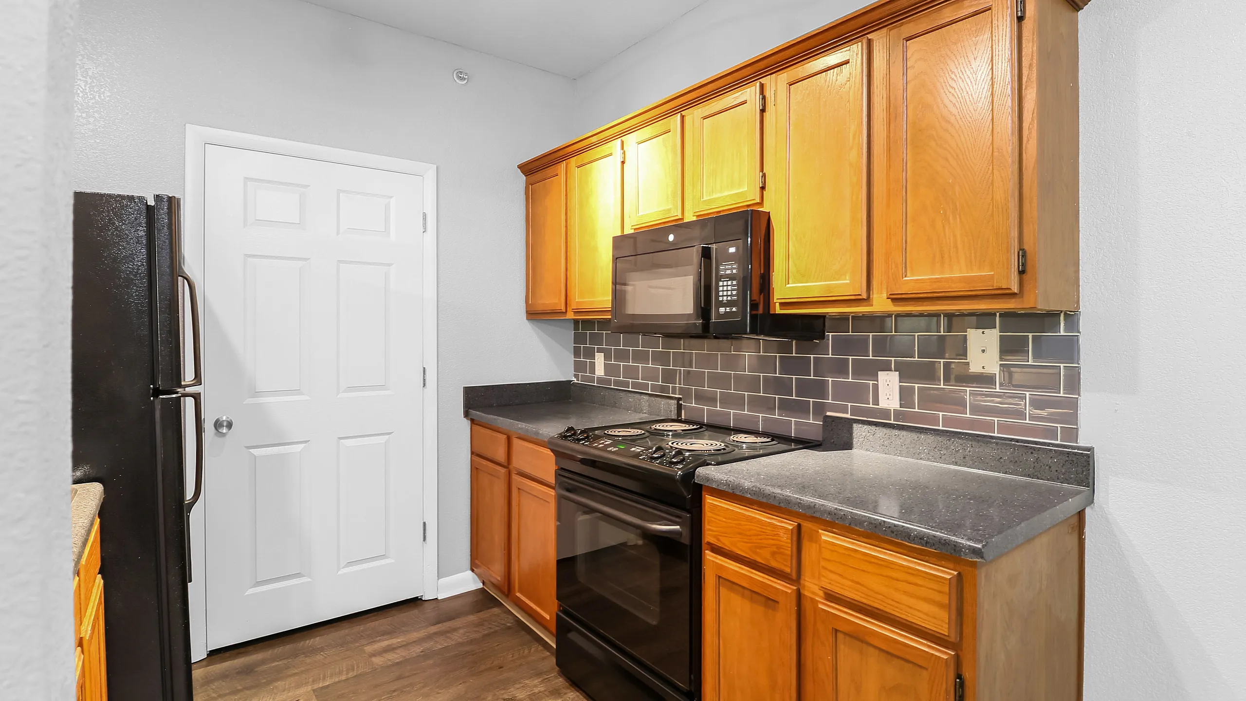 Modern kitchen with sleek black appliances, warm wooden cabinetry, and stylish tile backsplash, offering a welcoming culinary space.