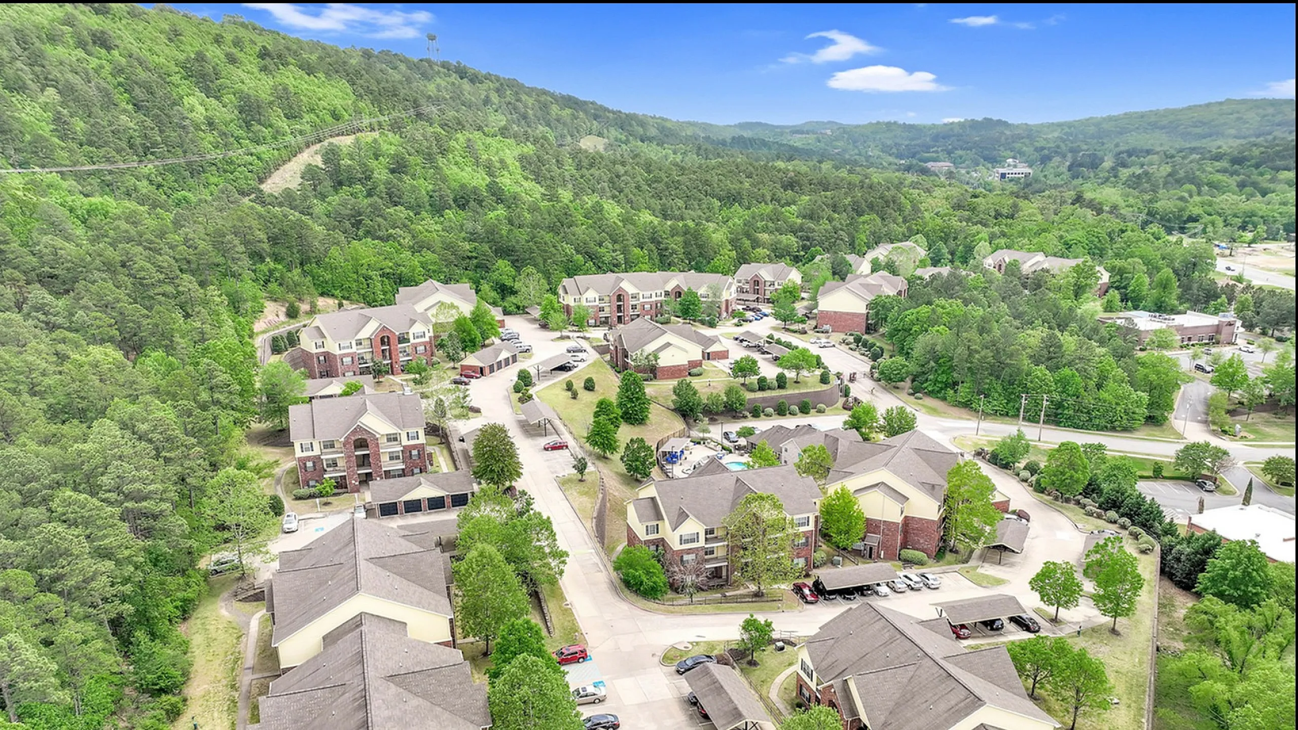 Scenic aerial view of a tranquil apartment complex nestled in lush greenery, offering a serene living environment surrounded by hills and vibrant nature.
