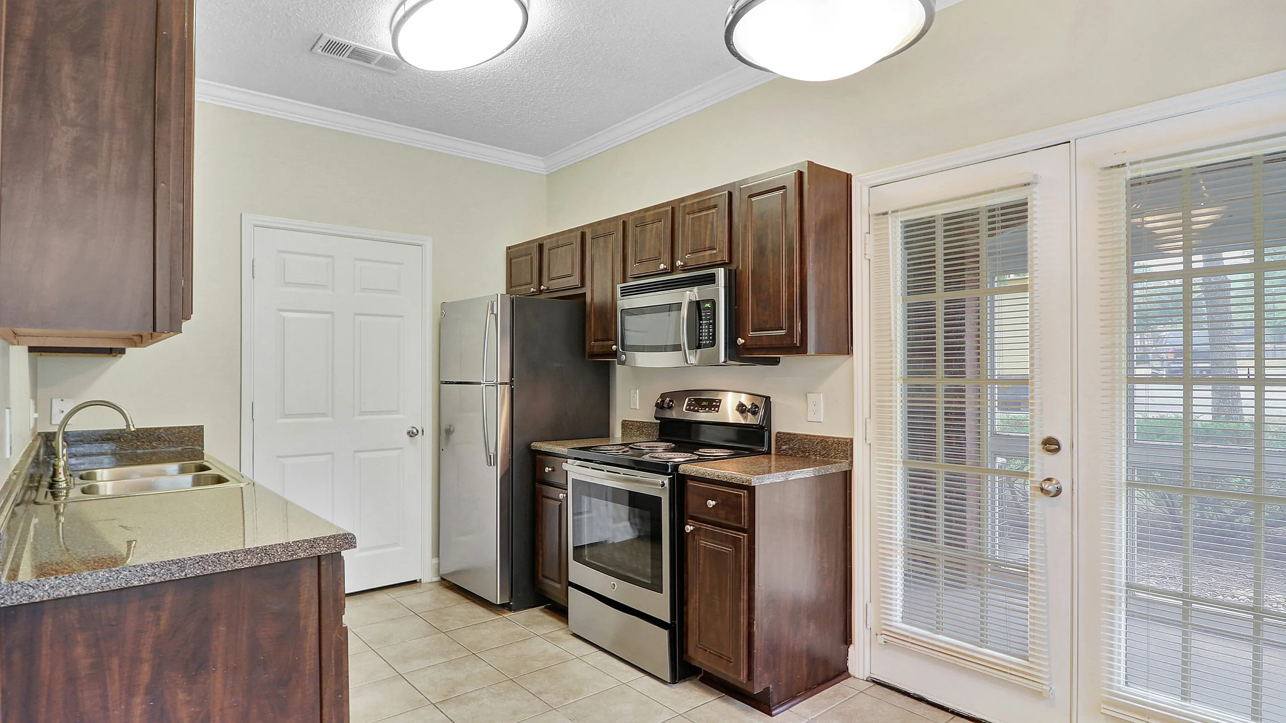 Modern kitchen with sleek stainless steel appliances, dark wood cabinets, and elegant French doors opening to a bright outdoor view.