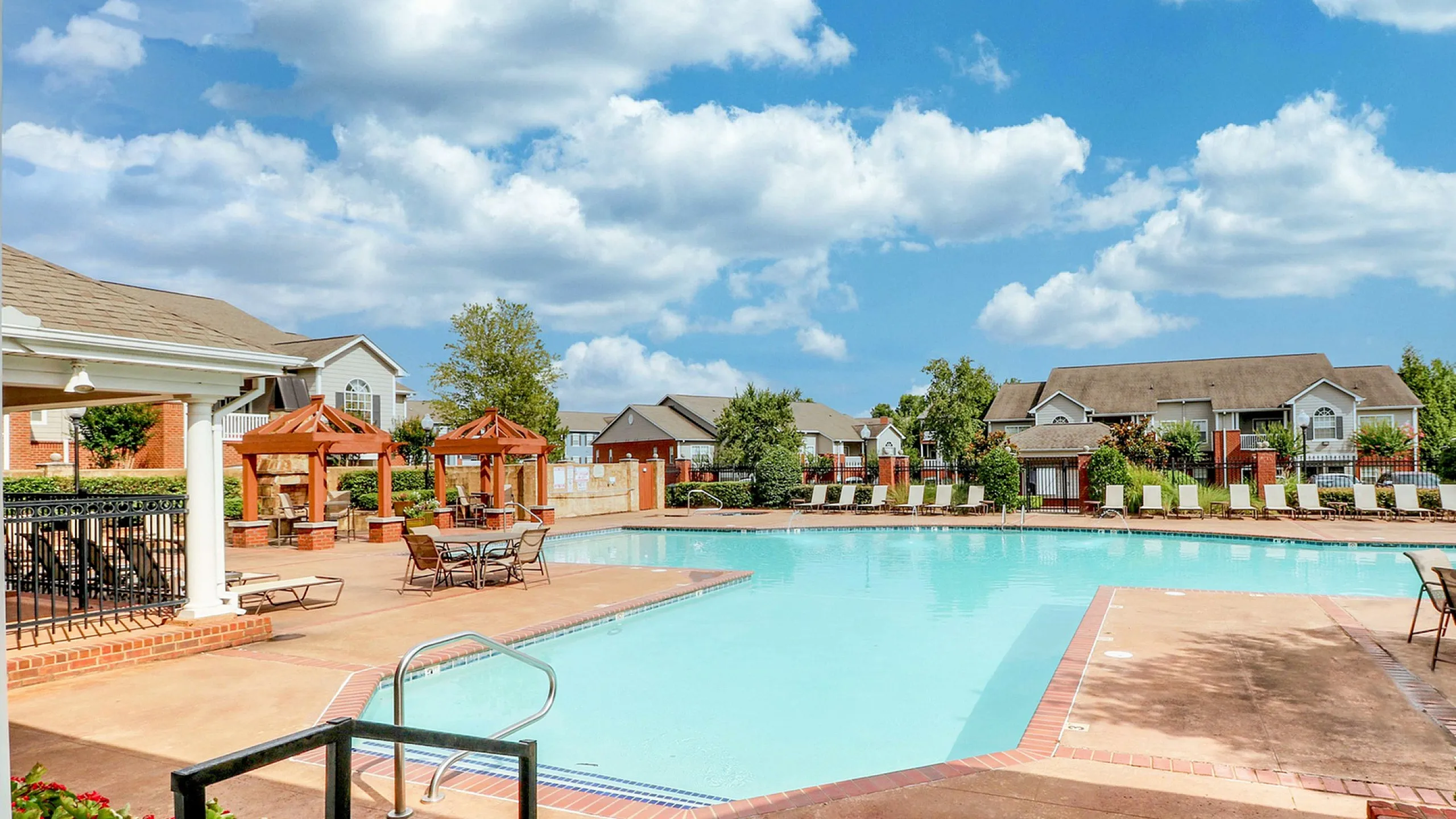 Resort-style community pool area with inviting cabanas, modern seating, and charming residential backdrop under a clear blue sky.