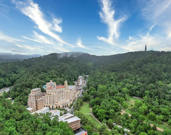 Breathtaking aerial view of a historic building nestled amid lush green mountains under a vibrant blue sky.