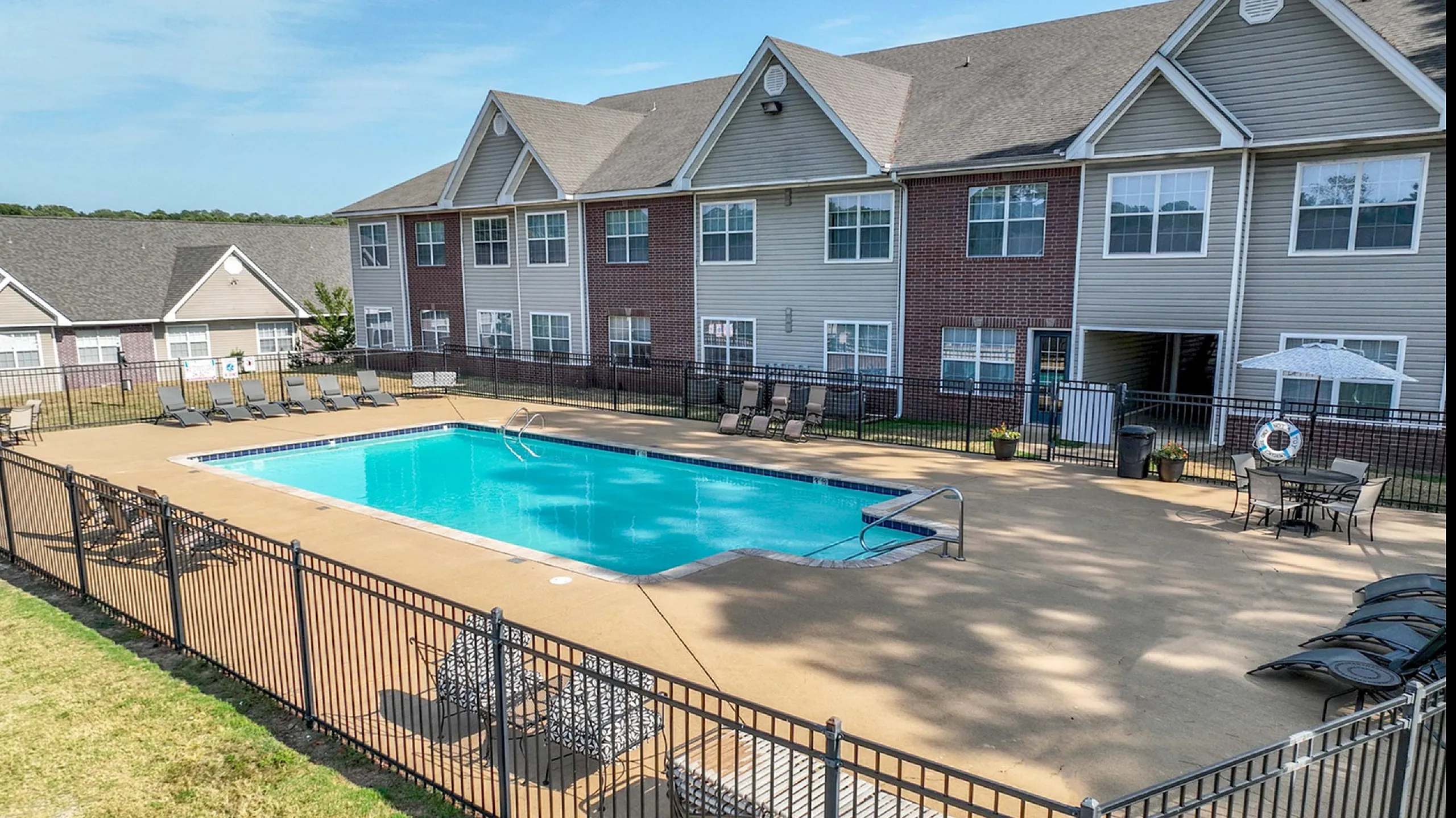 Inviting community pool area surrounded by sun loungers, set against a backdrop of charming modern apartments.