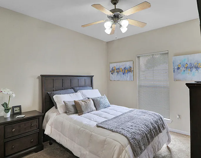 Elegant bedroom featuring a cozy bed with plush pillows, stylish artwork, and a modern ceiling fan.