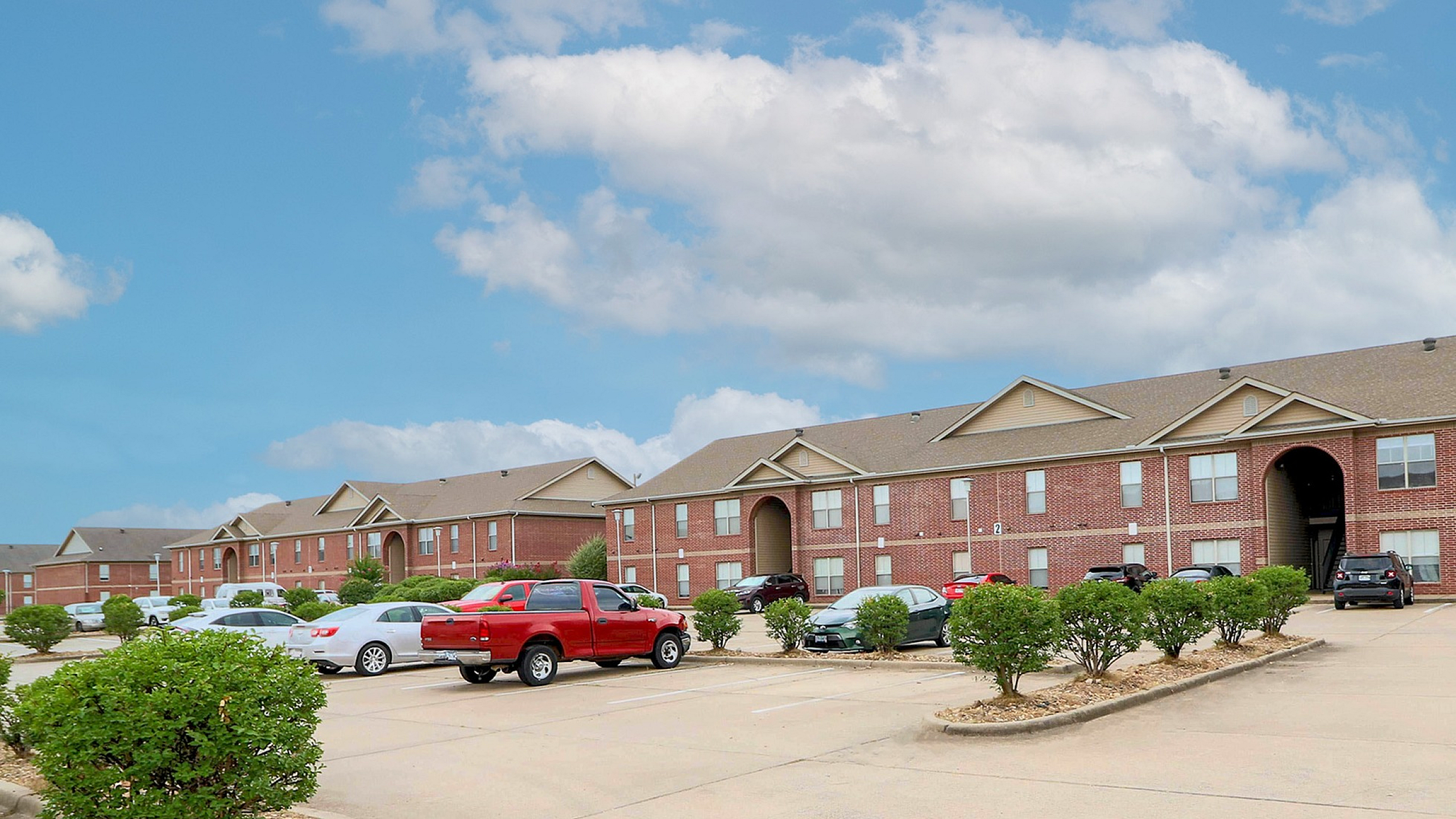 Charming red-brick apartment complex with ample parking, nestled under a bright blue sky.