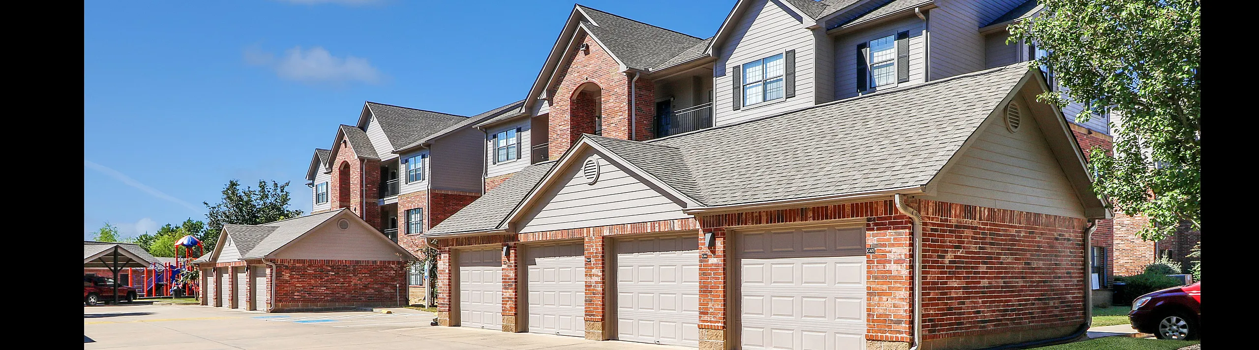 Charming townhouse complex with red brick exteriors, private garages, and sunny, tree-lined surroundings.