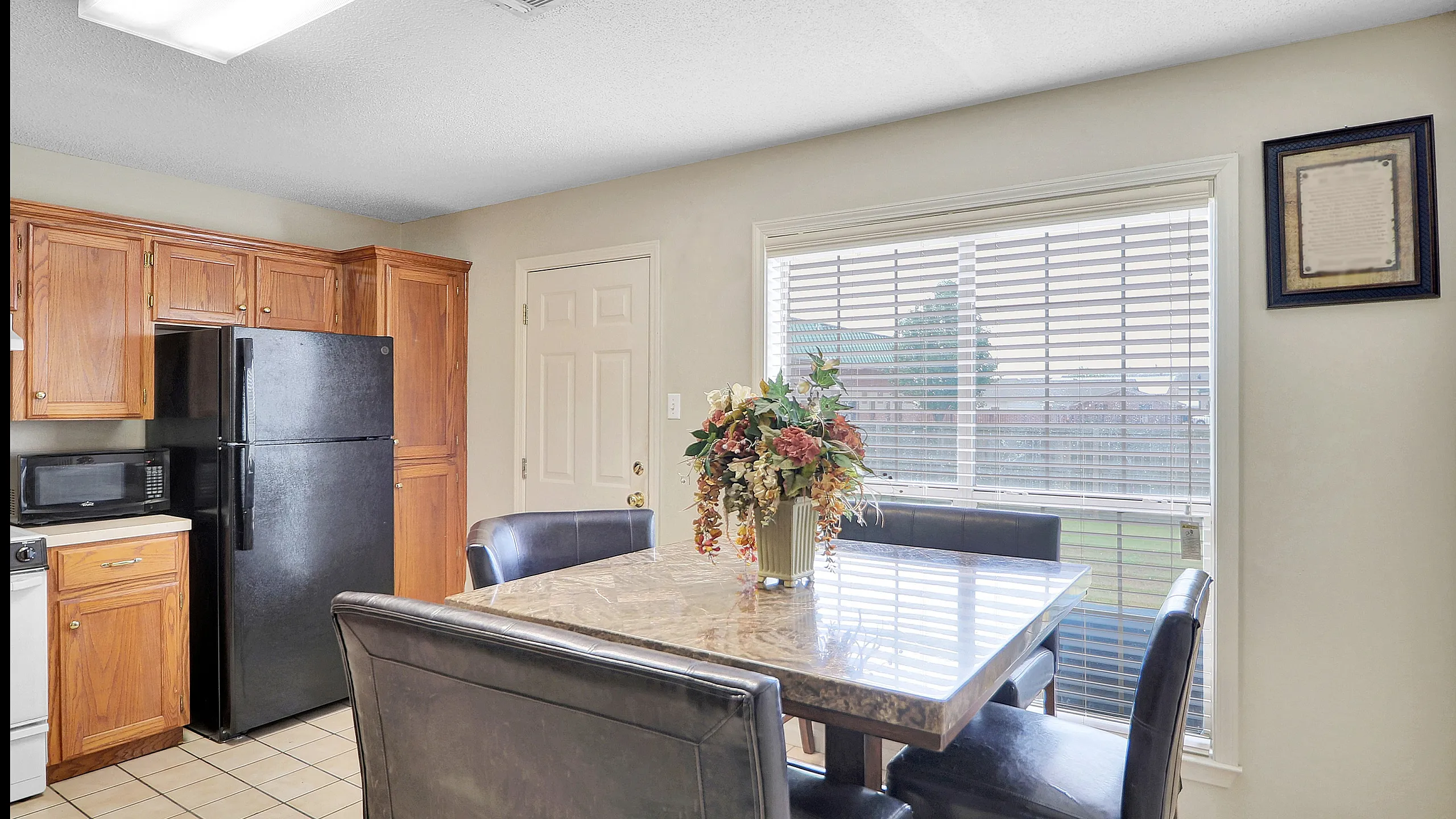 Inviting kitchen with warm wood cabinets, sleek black appliances, and a sunlit dining area featuring a marble-top table and leather chairs.