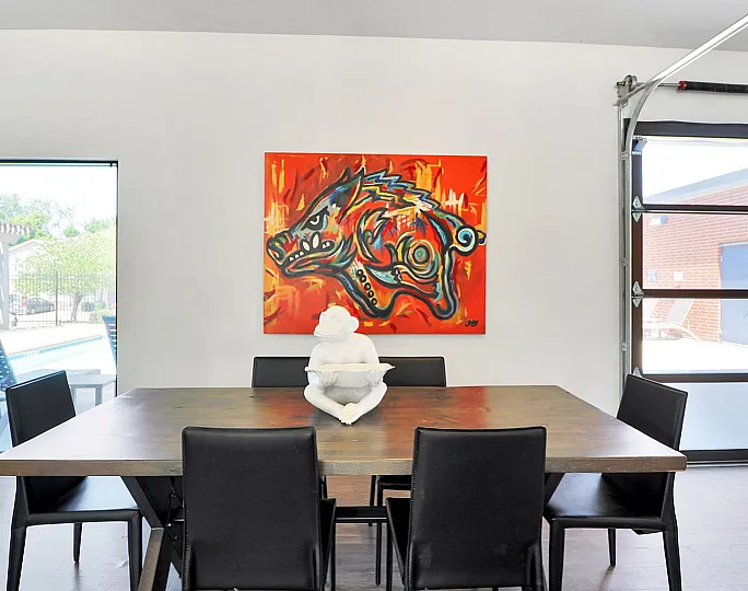 Contemporary dining area with vibrant artwork and chic decor, showcasing natural light through large windows.