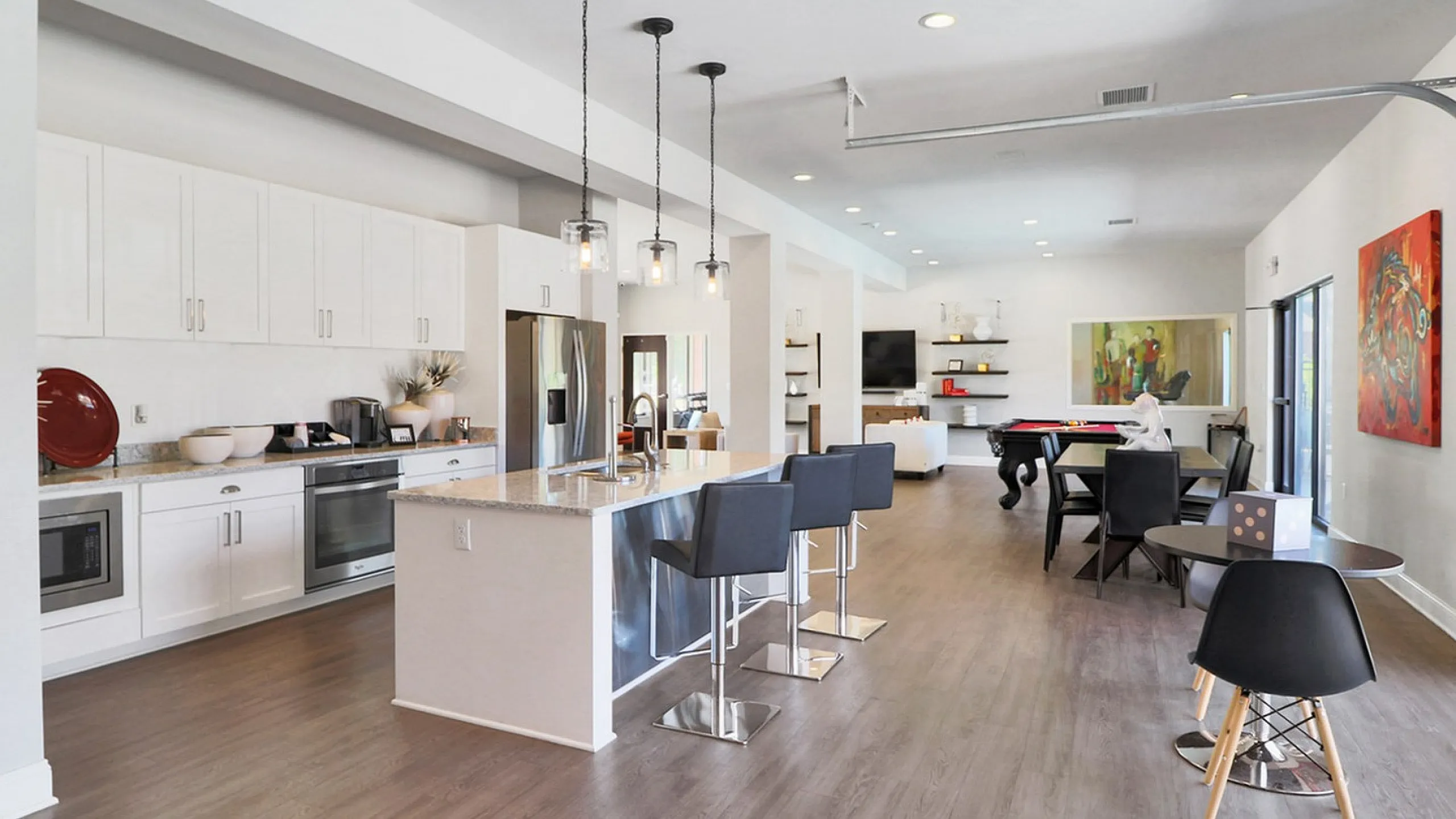 Modern open-concept kitchen and living space featuring sleek white cabinets, a stylish kitchen island with bar stools, and elegant wood flooring.