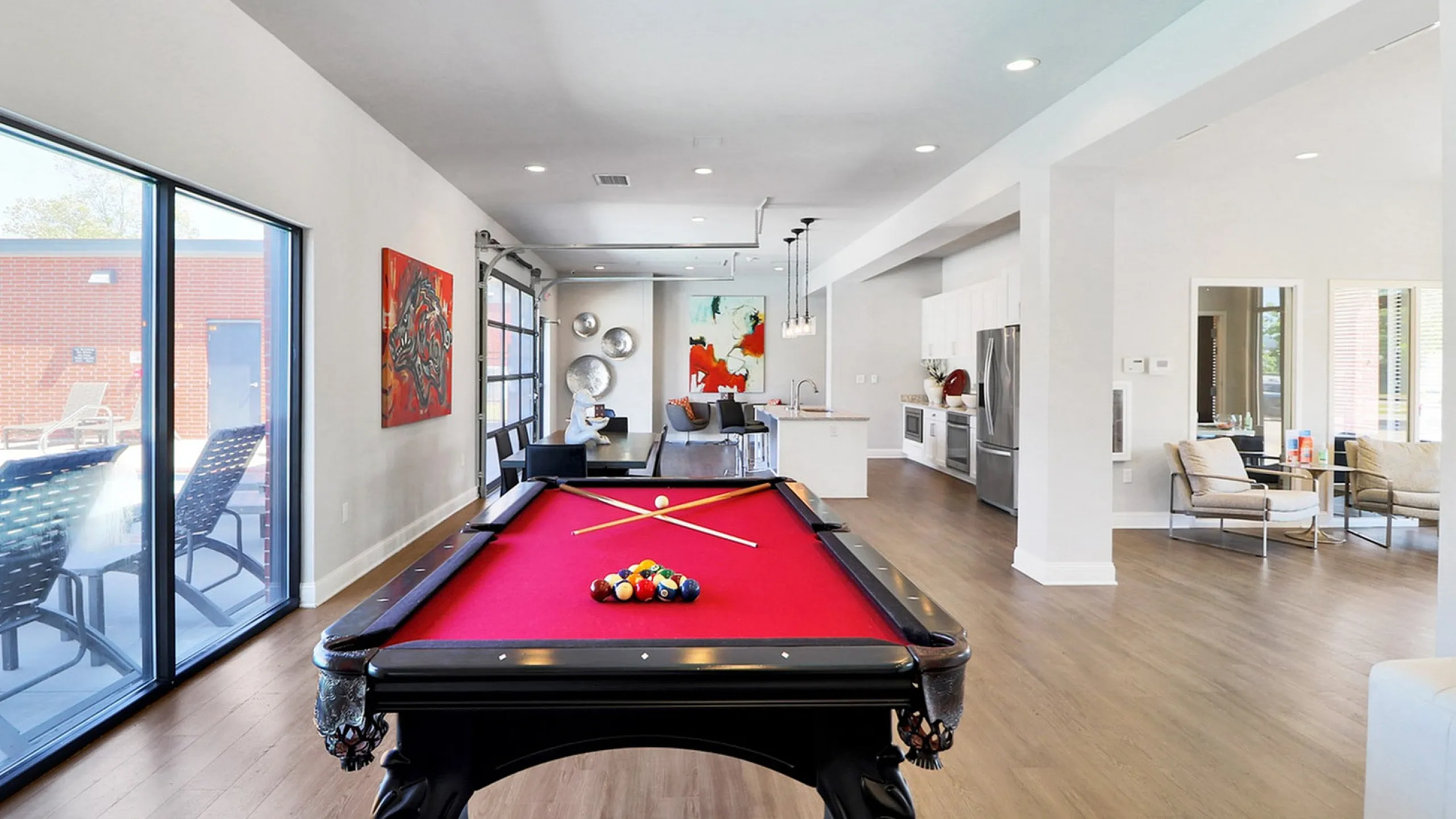 Modern open-concept apartment featuring a luxurious red pool table, stylish kitchen, and vibrant artwork, perfect for entertainment and relaxation.
