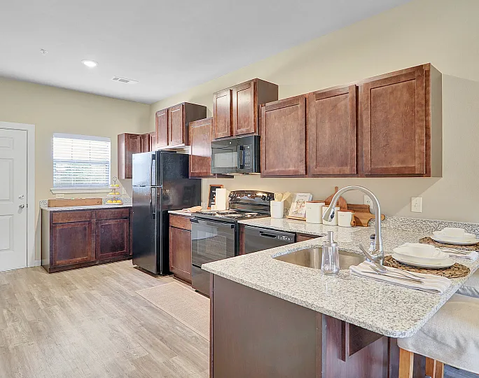 Modern kitchen with sleek granite countertops, rich wooden cabinetry, and a cozy breakfast bar. Equipped with stainless steel appliances, including a fridge and microwave, offering a warm and inviting atmosphere.