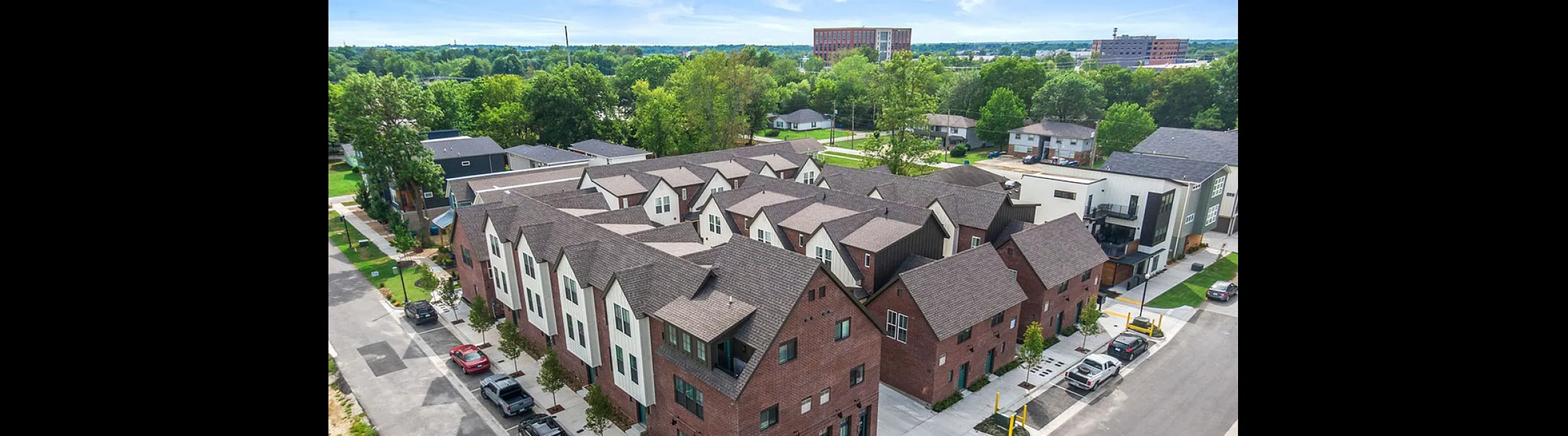 Charming residential complex with modern red-brick townhouses surrounded by lush greenery and a vibrant neighborhood view.