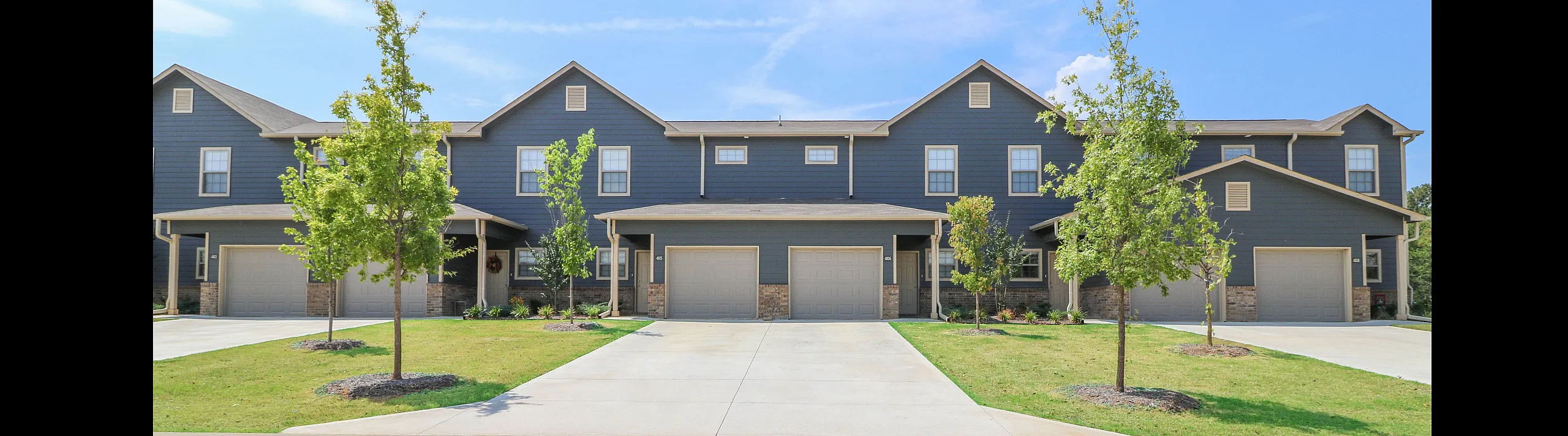 Charming townhouse complex featuring modern architecture, manicured lawns, and private driveways under a clear blue sky.