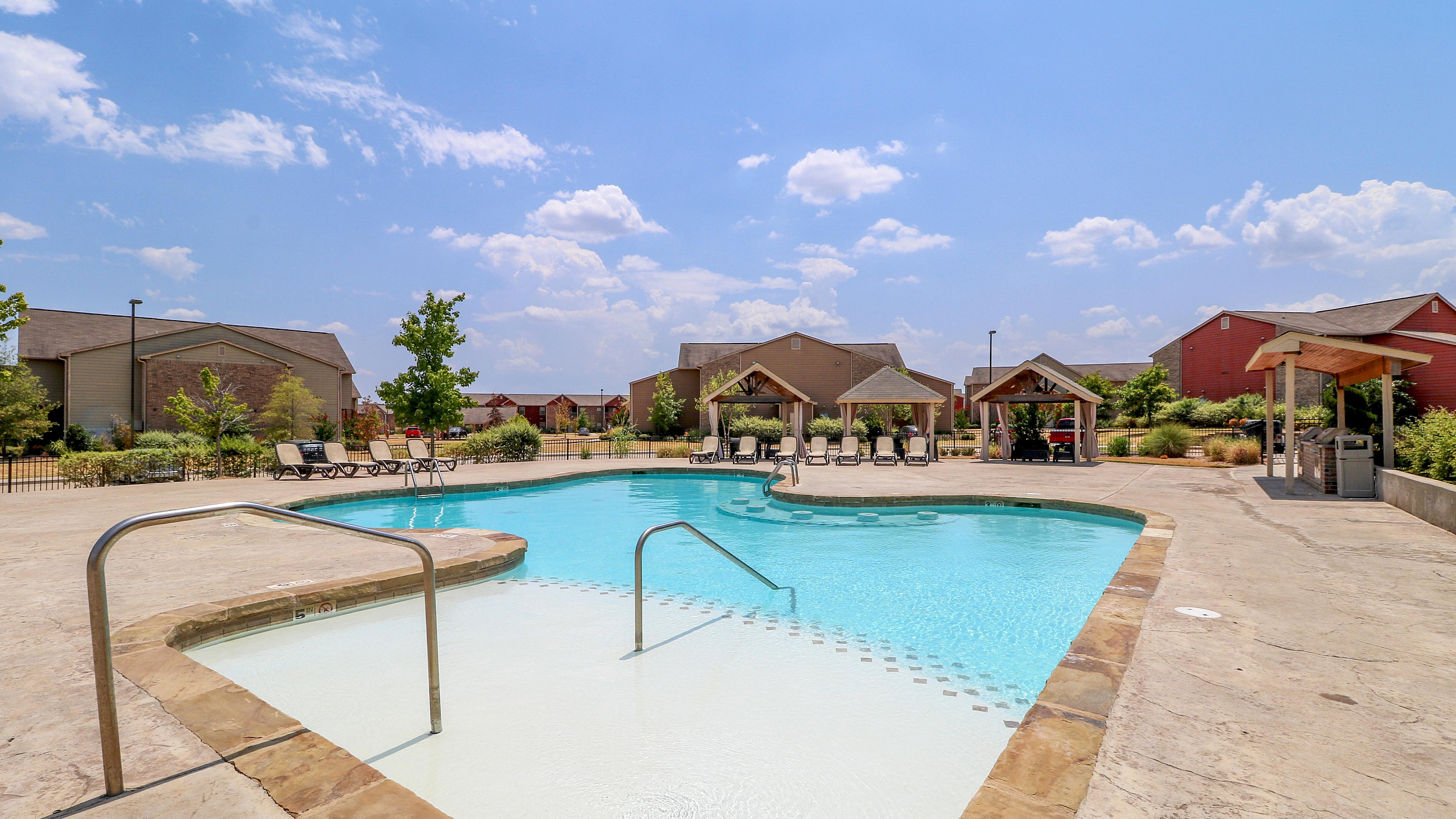 Inviting outdoor pool area with sun loungers and shaded cabanas under a clear blue sky, perfect for relaxation and leisure.