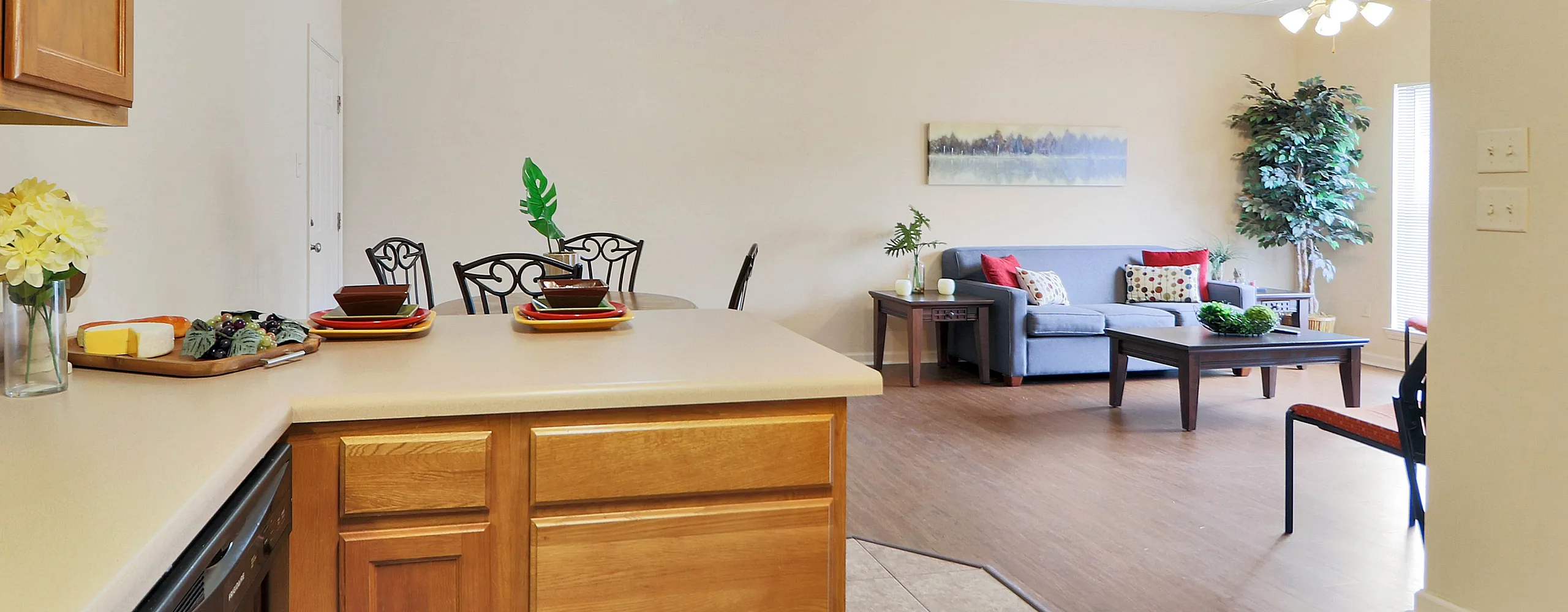 Bright and inviting open-concept living area featuring a cozy kitchen with wooden cabinets, elegant dining set, and stylish living room with vibrant accents.