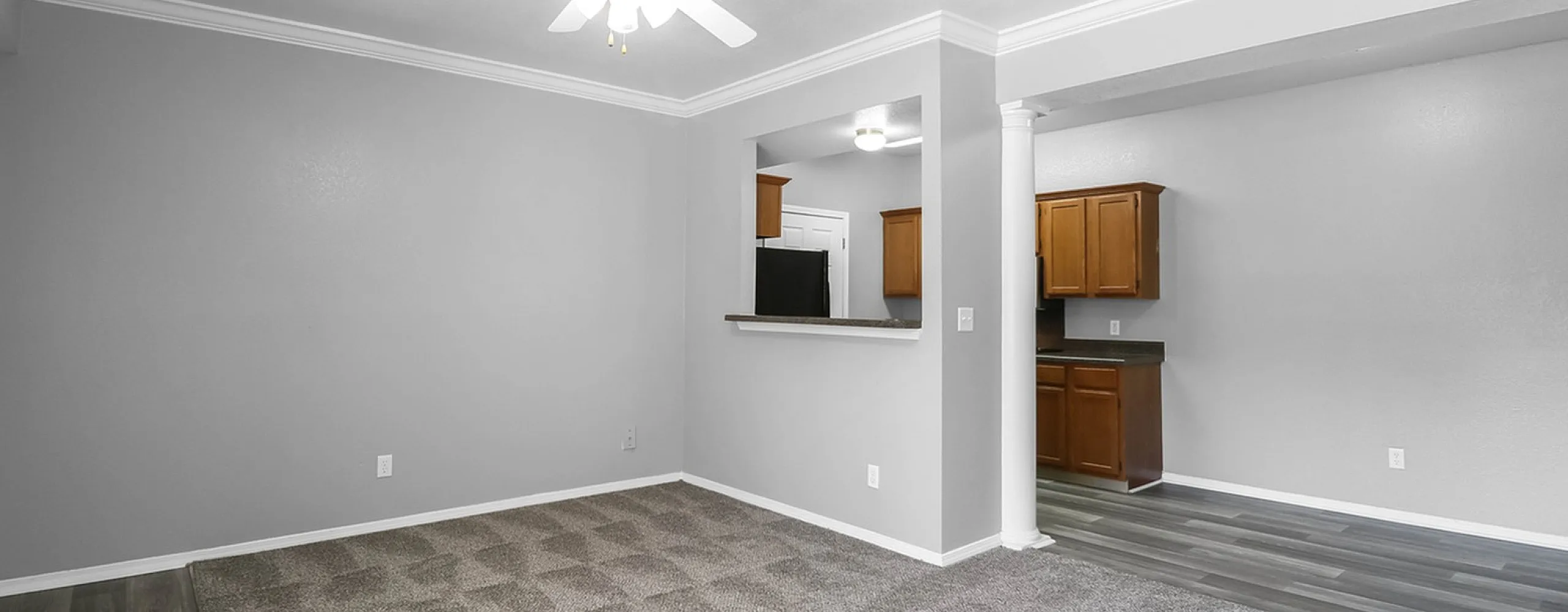 Elegant living room with plush carpet and open layout, featuring a view into a modern kitchen with wood cabinetry and stylish flooring.