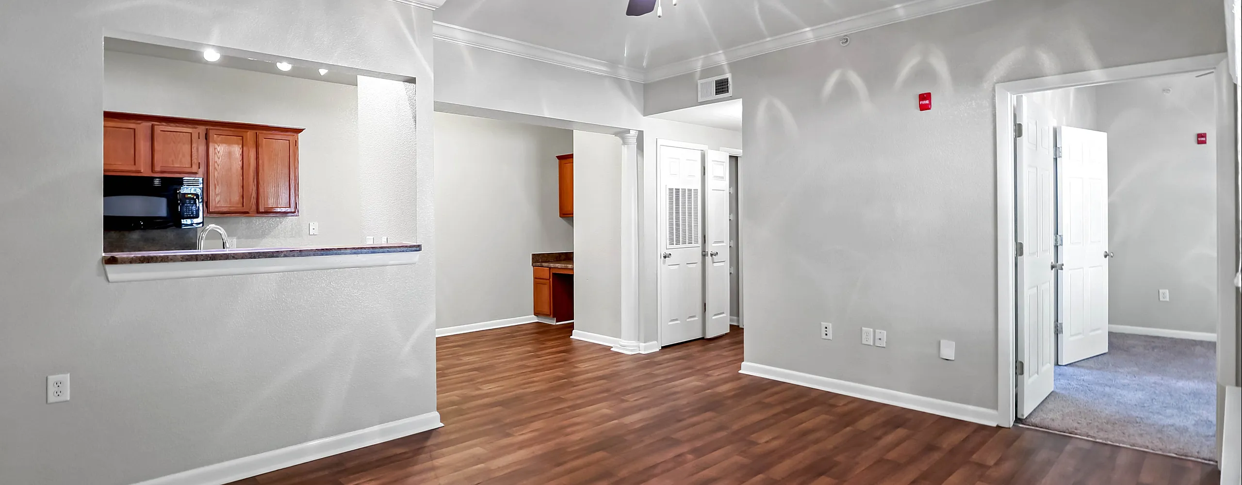 Inviting apartment interior featuring sleek hardwood floors, bright open spaces, and a modern kitchen with wooden cabinetry and black appliances.