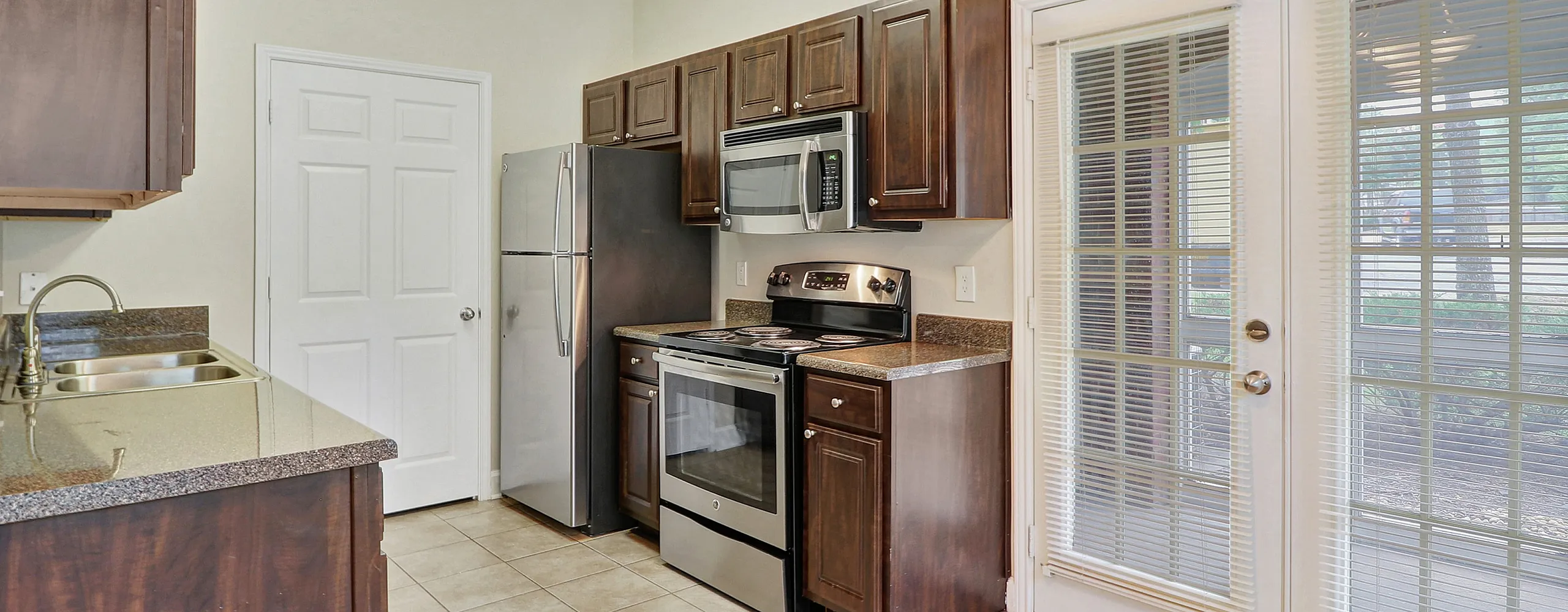 Modern kitchen with stainless steel appliances, elegant dark wood cabinets, and natural light from French doors.