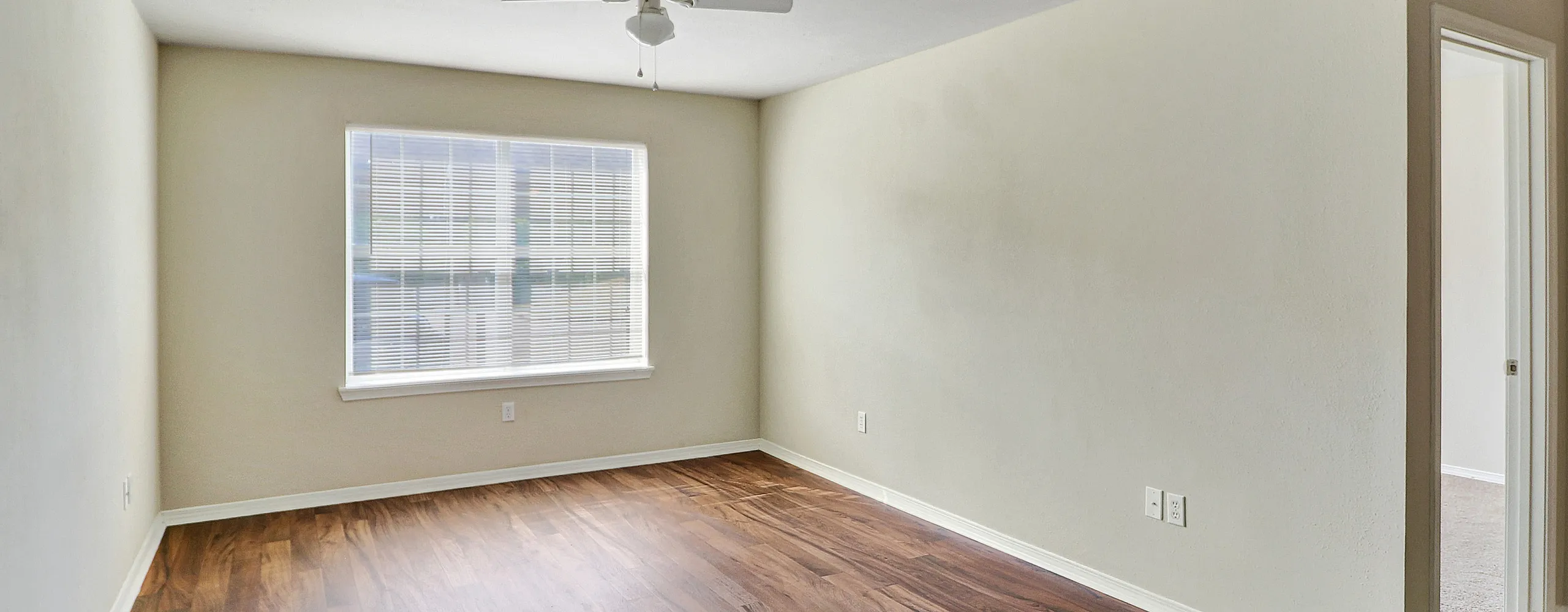 Bright and airy room with elegant wood flooring, large window, and ceiling fan; perfect for a modern living space.