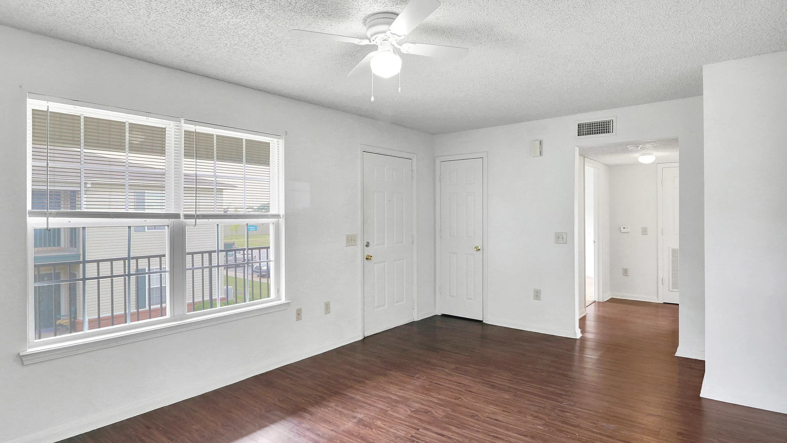 Bright living room with elegant wood flooring, large windows, and a ceiling fan, enhancing the open and airy space.