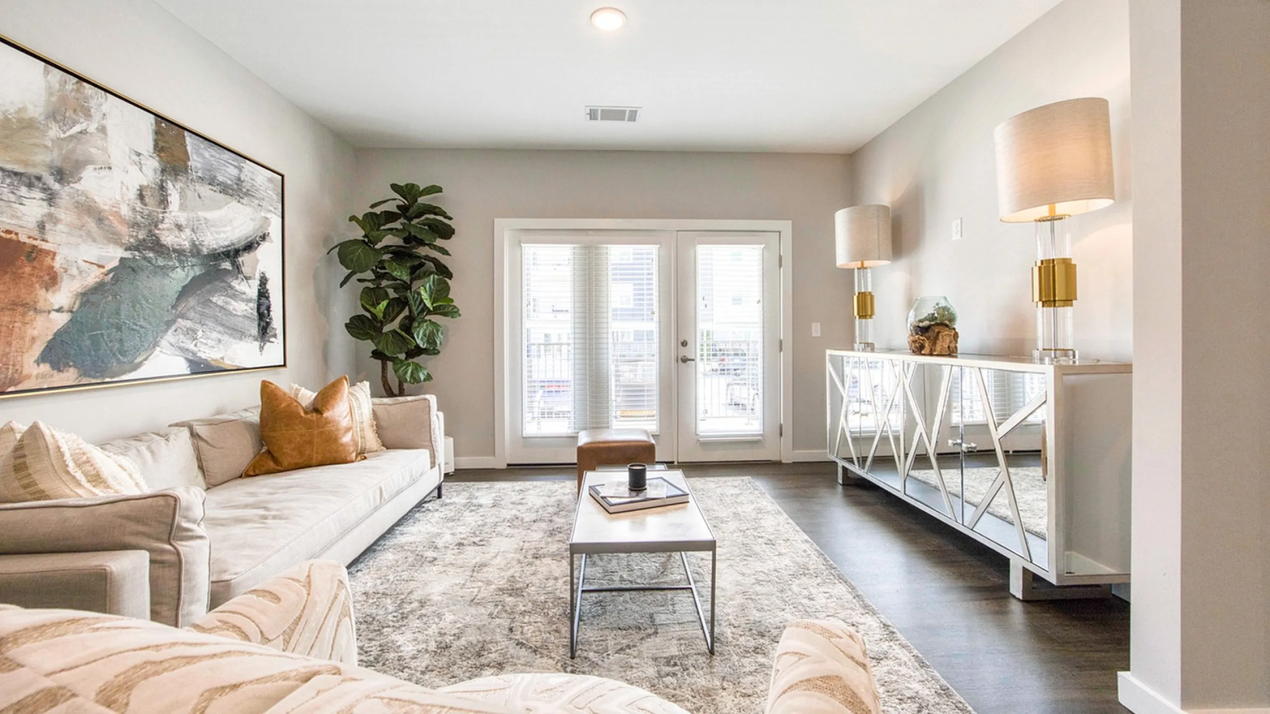 Elegant living room with chic decor, featuring plush sofas, a bold abstract painting, and stylish floor lamps, filled with natural light.